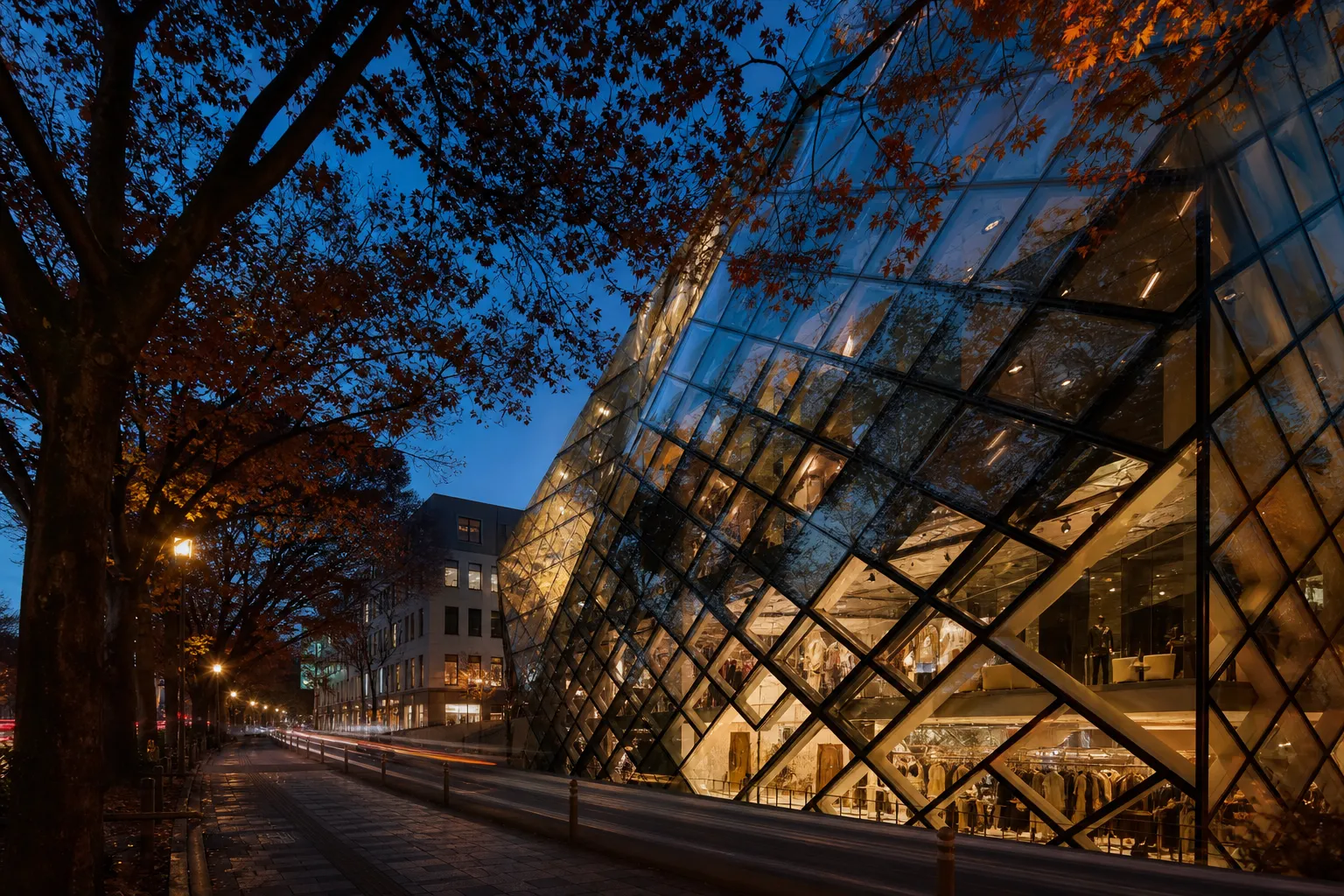 A sleek, geometric glass boutique building in Omotesando during twilight, showcasing modern Japanese architectural innovation and the sophisticated, tree-lined atmosphere of Tokyo's