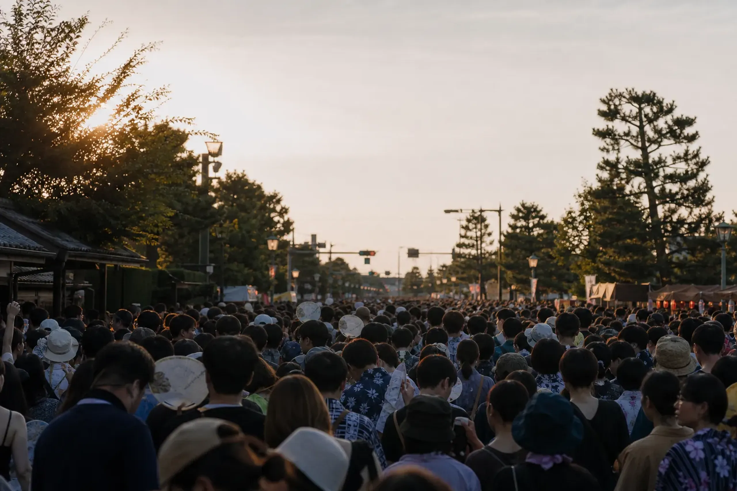 Dense summer matsuri crowd with people using handheld fans and drinking water in early evening heat