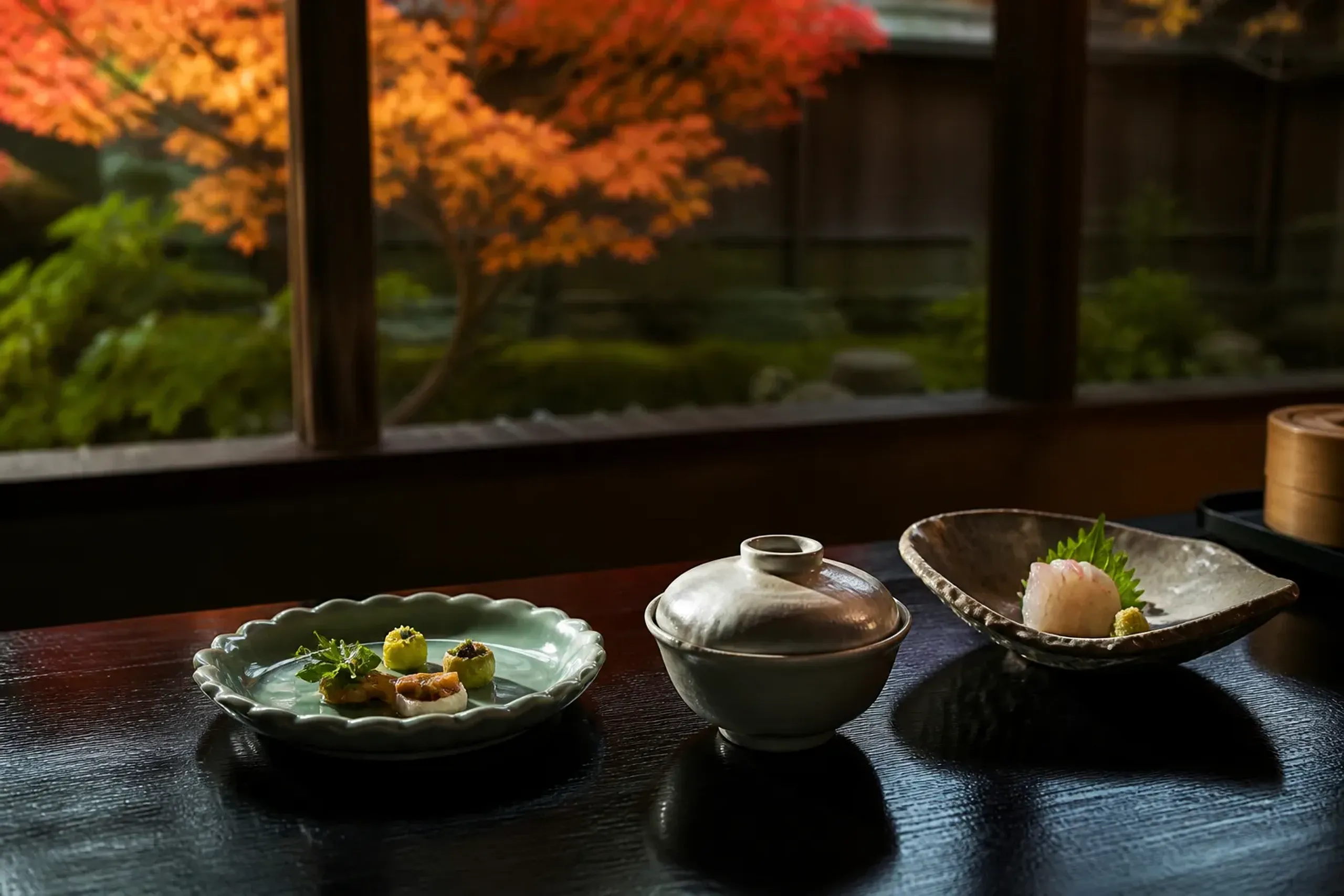 Seasonal Japanese kaiseki course plated on ceramic dishes on a dark lacquered table