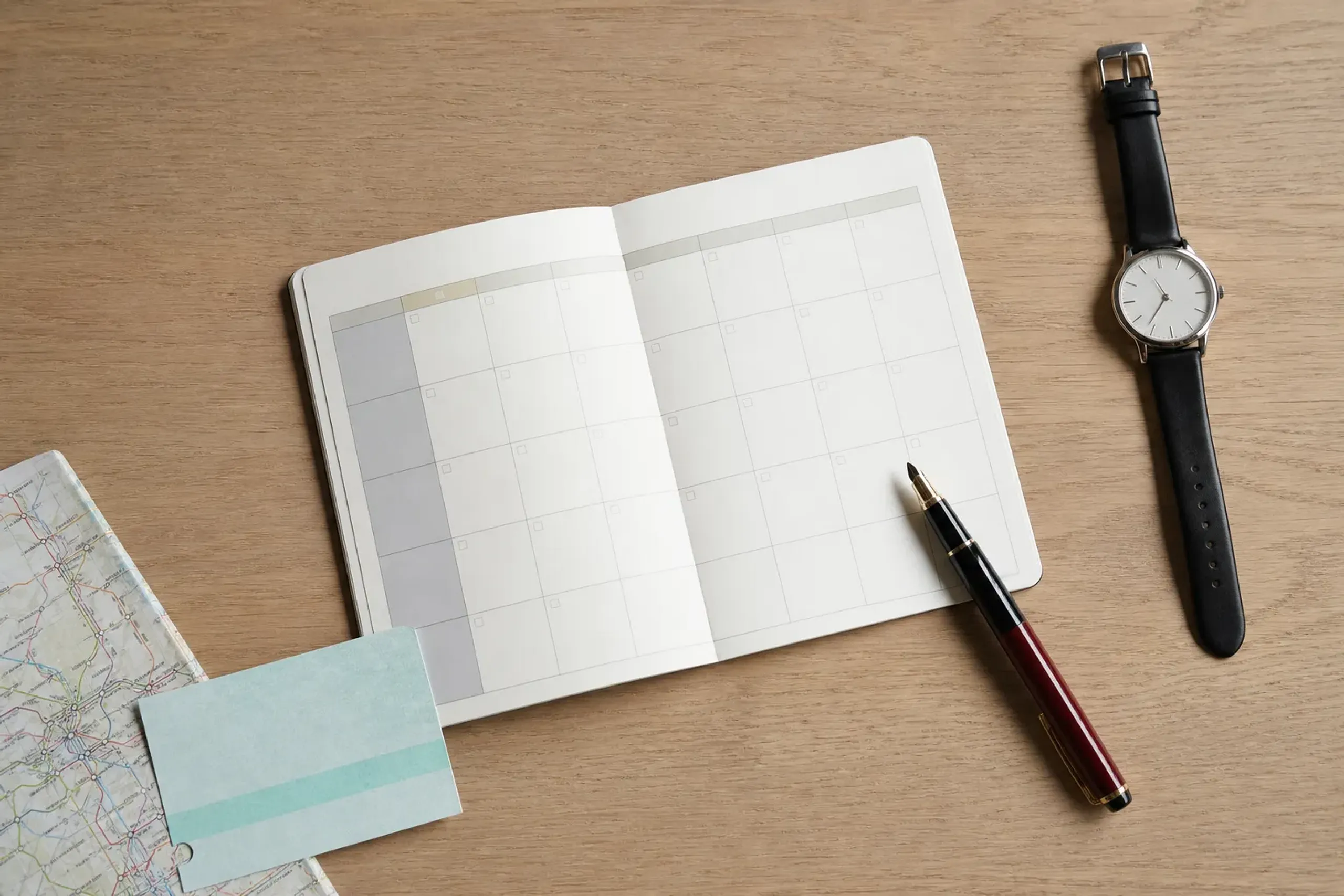 Calendar and pen on a wooden table with rail travel items, suggesting pre-trip planning