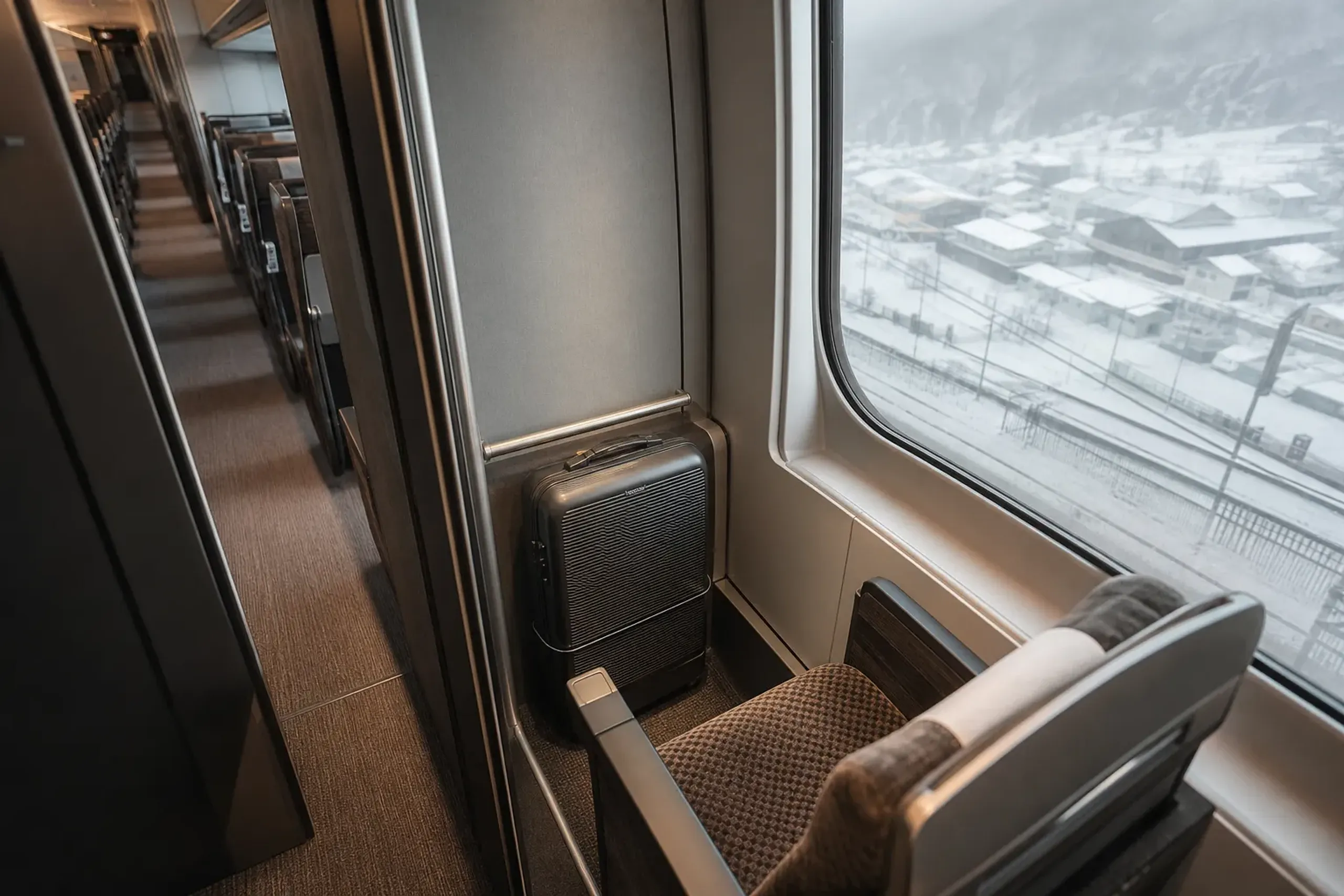 a reserved oversized-baggage compartment seat at the rear of a Tokaido Shinkansen car, with a single slim forward-shipped suitcase stowed neatly in the designated space