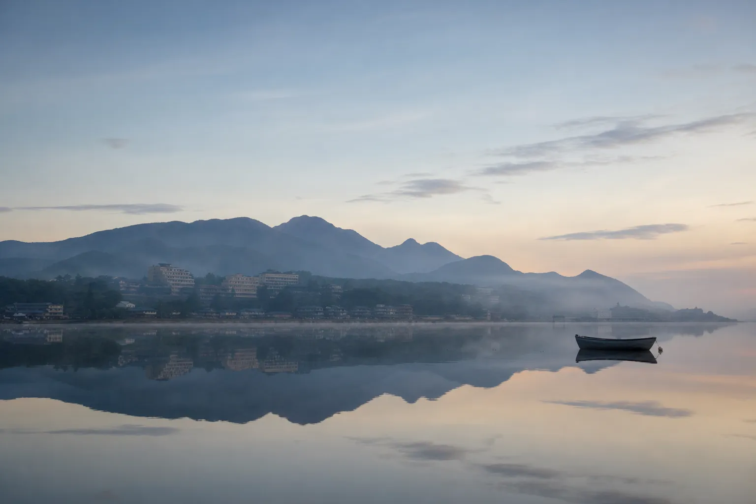 the still shoreline of Lake Biwa in Shiga Prefecture at dawn, with calm water reflecting the distant mountains and a quiet lakeside town