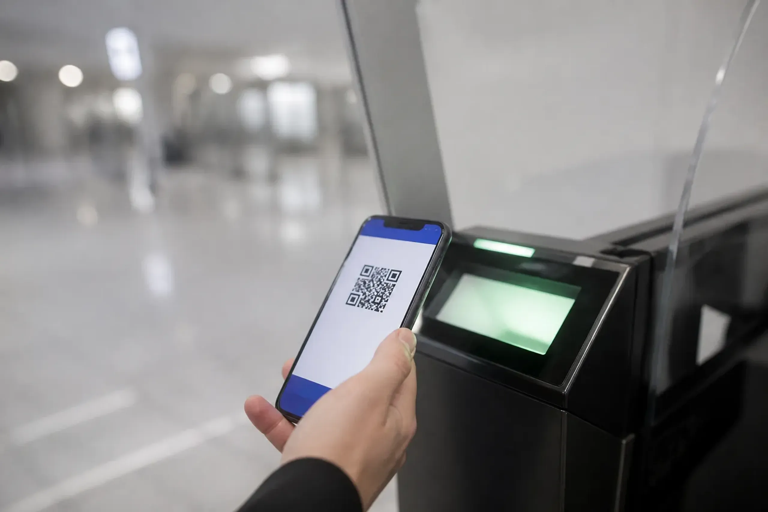 a smartphone displaying a Visit Japan Web QR code held up at an automated e-Gate immigration kiosk in a Japanese international airport arrivals hall