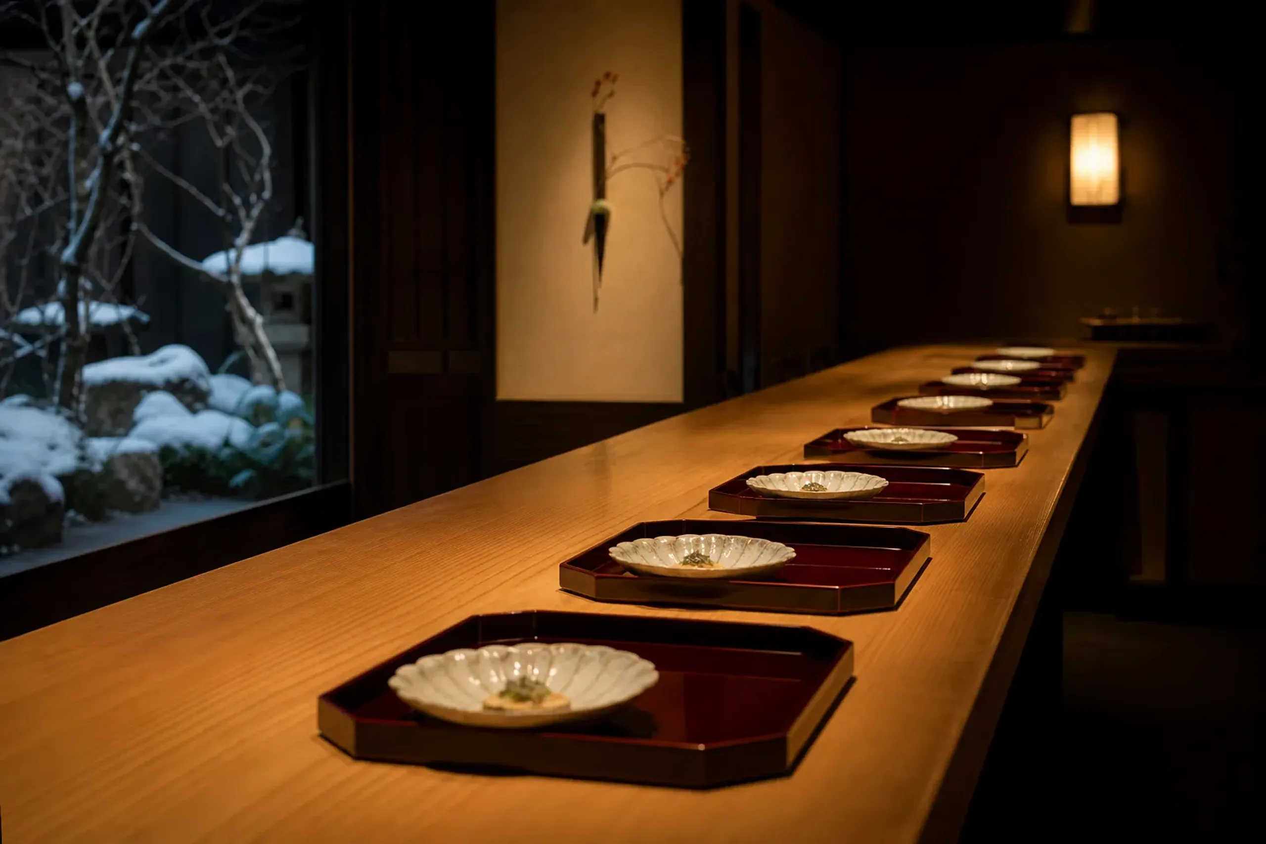 An intimate eight-seat kaiseki counter of polished hinoki cypress wood in a Kyoto ryokan, set with lacquered trays and seasonal ceramics under warm lantern light