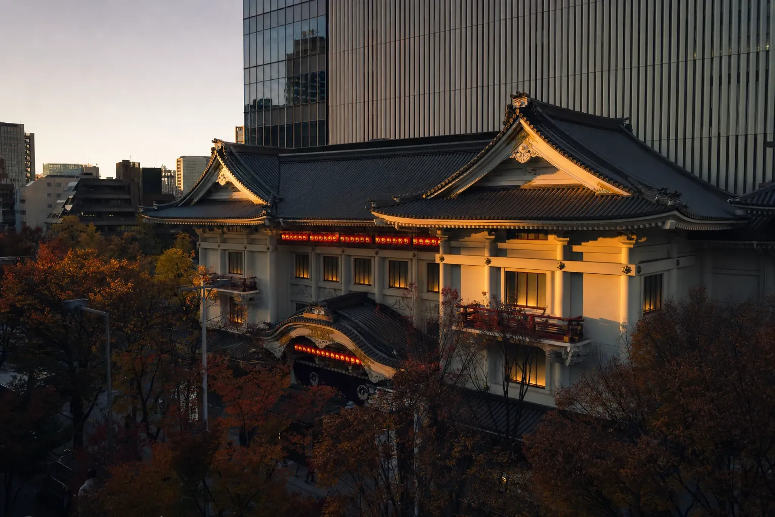 The traditional gabled façade of the Kabukiza theater in Ginza with its rows of red paper lanterns against the modern glass tower rising behind it