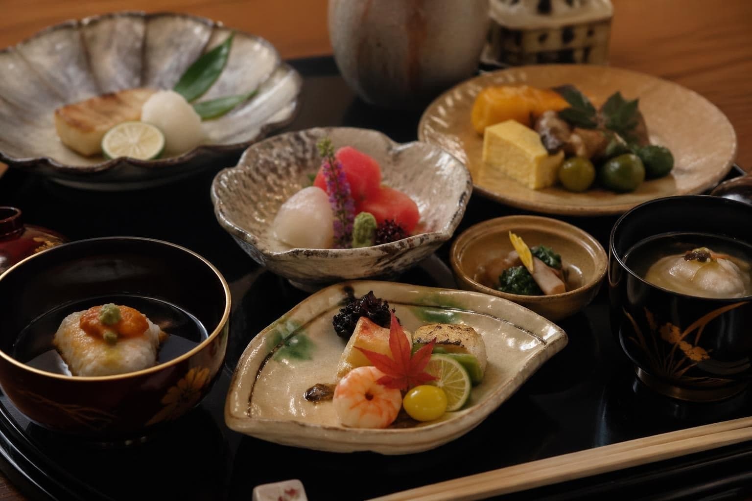 A kaiseki course arranged across handmade ceramics on a lacquer tray