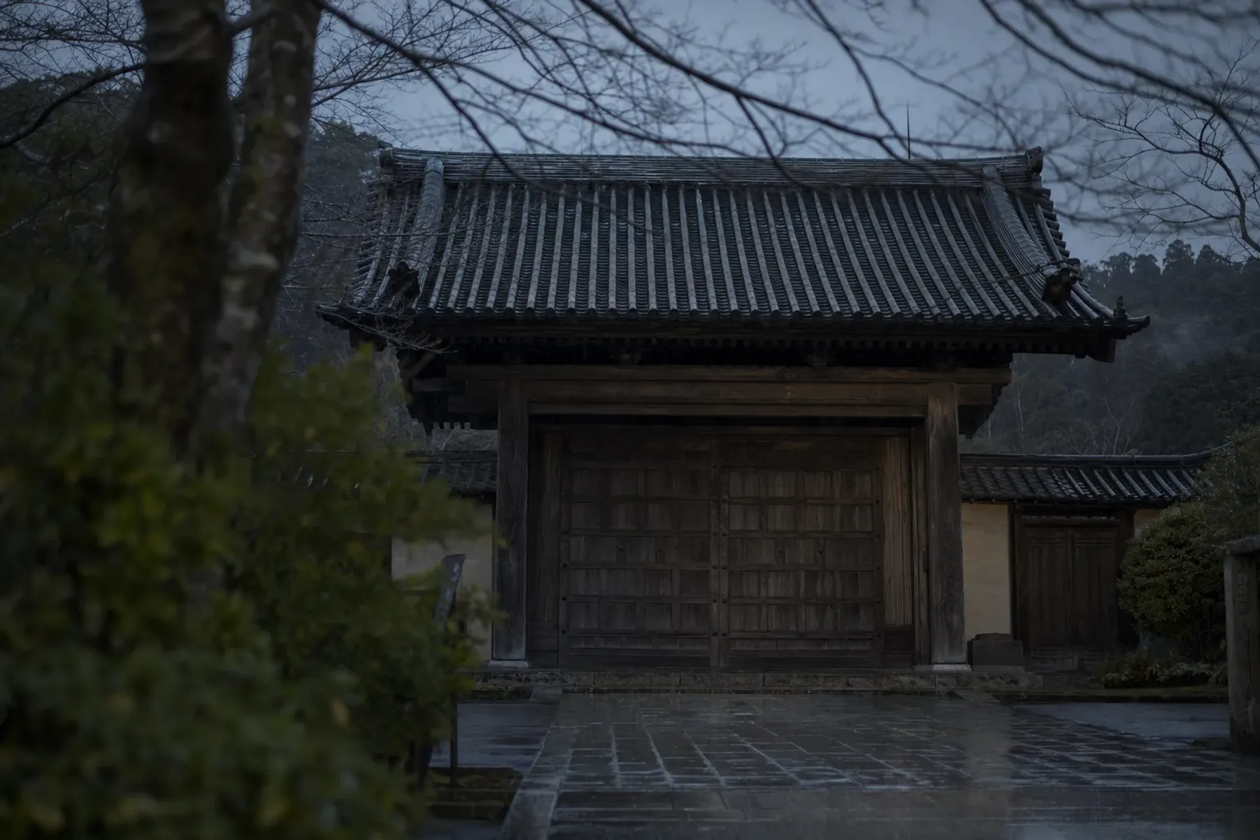 The closed wooden gate of Engaku-ji in Kita-Kamakura under a grey winter sky with sea wind stirring bare branches