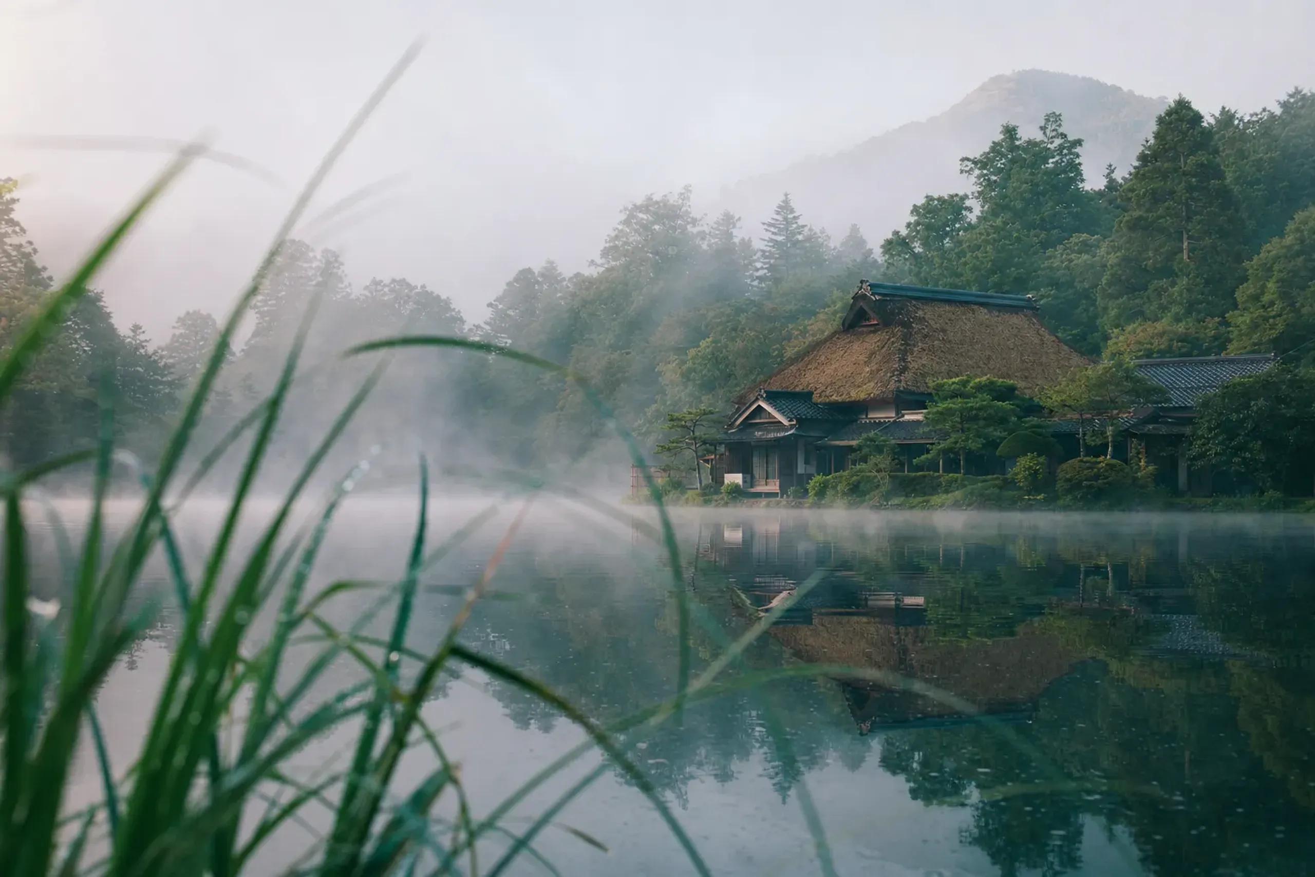 The distinctive roof structure of Yunotake-an restaurant at Kamenoi Besso, seen from across Kinrin Lake at the water's edge
