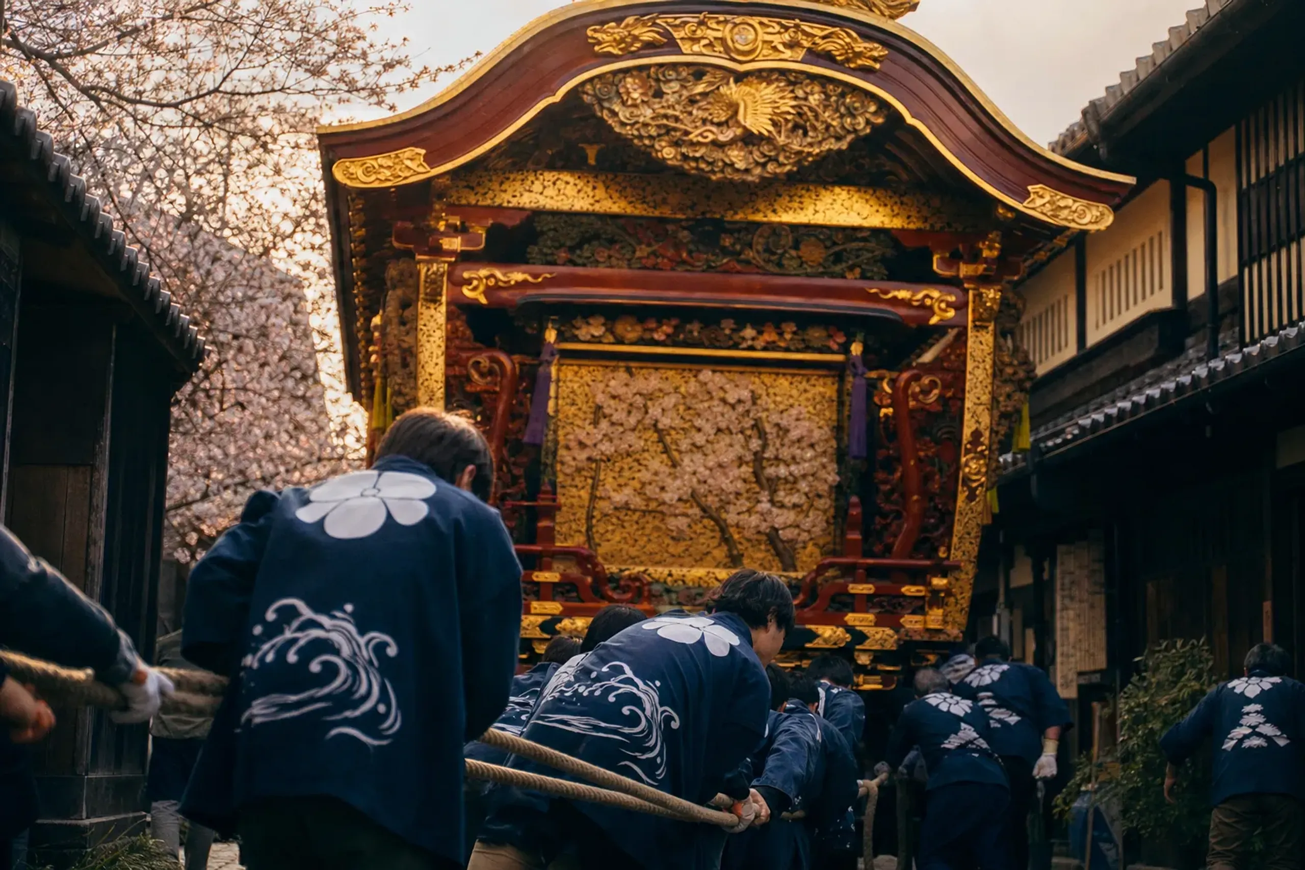 A towering seven-meter lacquered hikiyama float being pulled through the narrow streets of Karatsu City by its hauling team on the final day of Karatsu Kunchi, gold leaf catching the autumn light