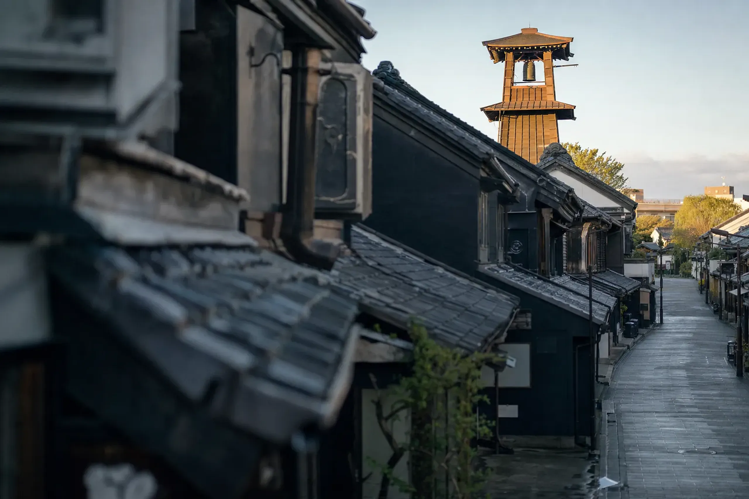 The wooden three-tiered yagura-style Toki no Kane bell tower rising above the Kurazukuri clay-walled warehouse rooftops in Kawagoe at soft early morning light