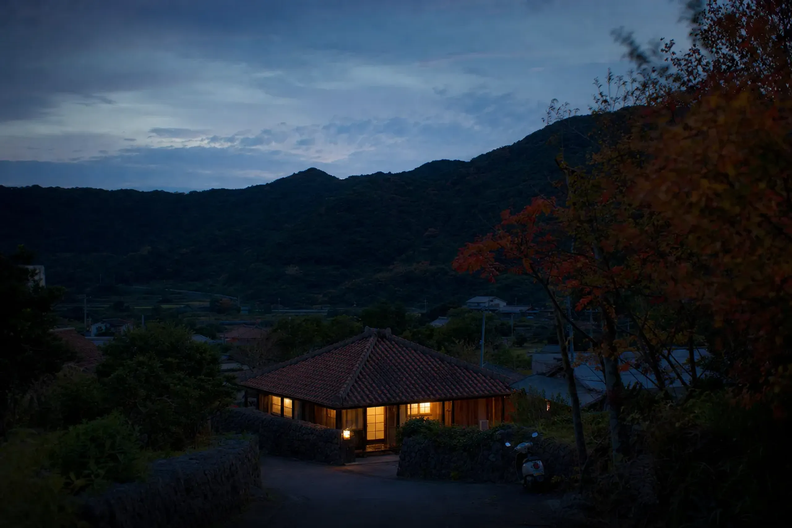 a quiet small-village guesthouse among green hills on Tokashiki Island at dusk
