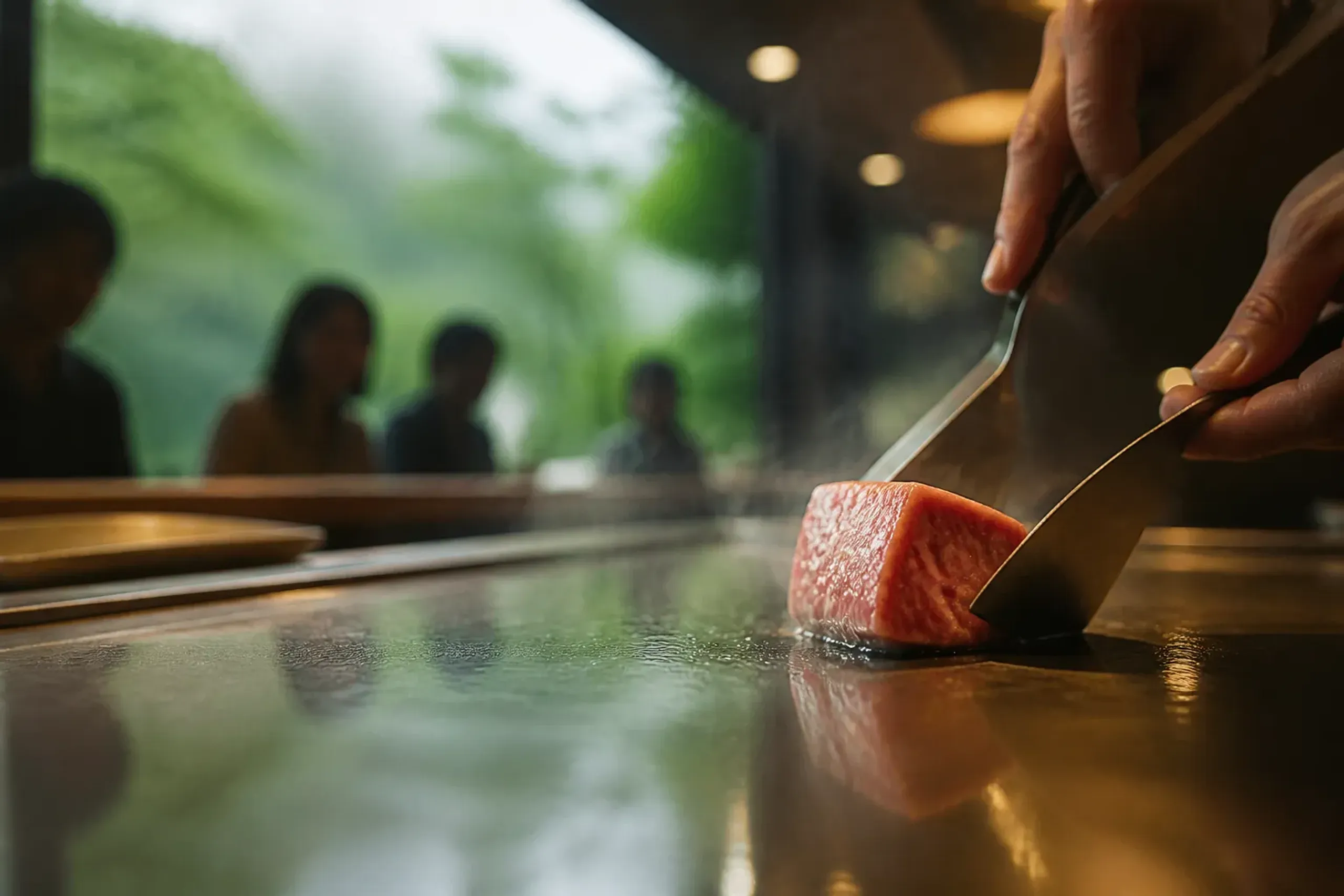 Chef searing small portions of marbled wagyu on a teppanyaki grill at a counter in Kobe