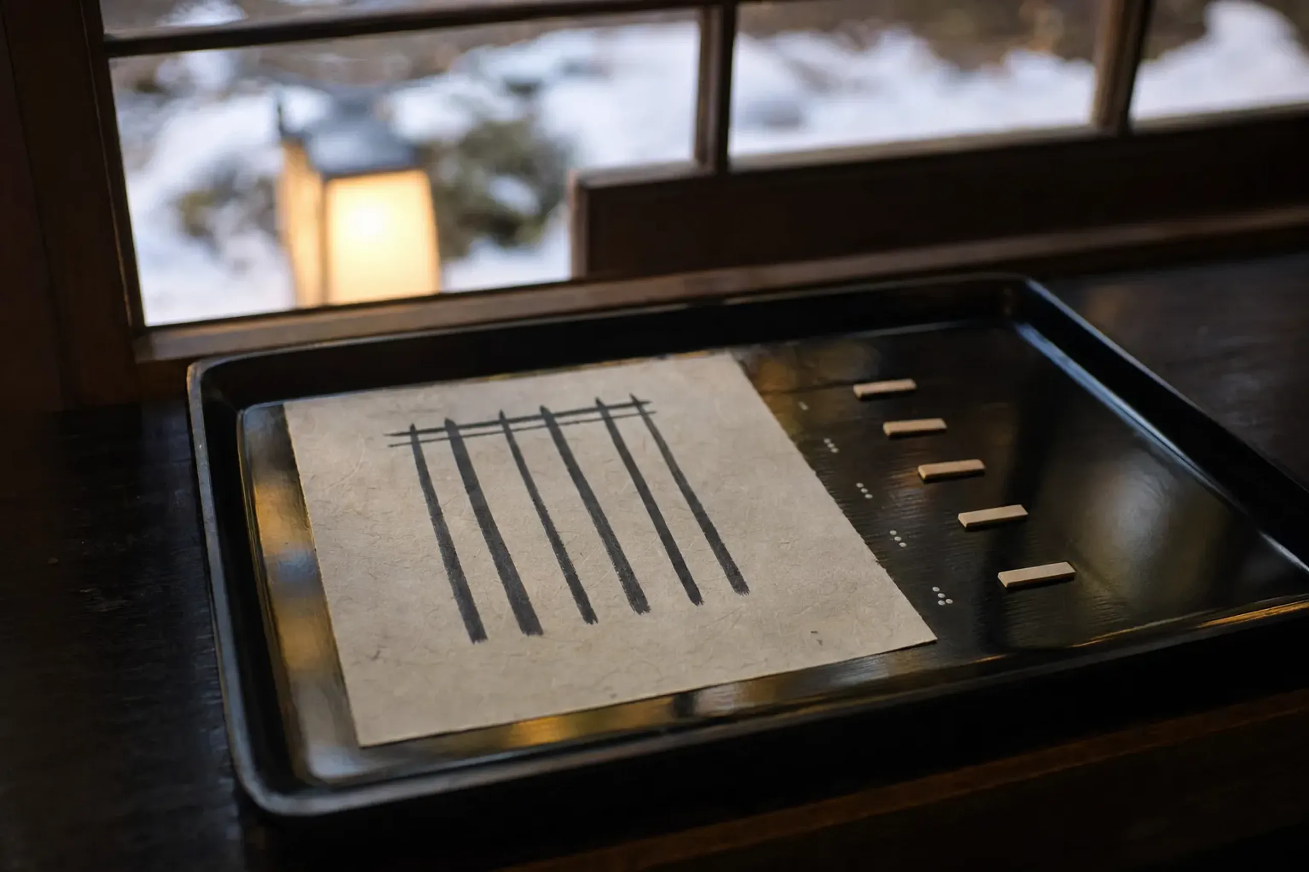 A sheet of washi paper marked with a Genji-kō symbol of five vertical lines linked at the top, arranged beside five numbered incense wood chips