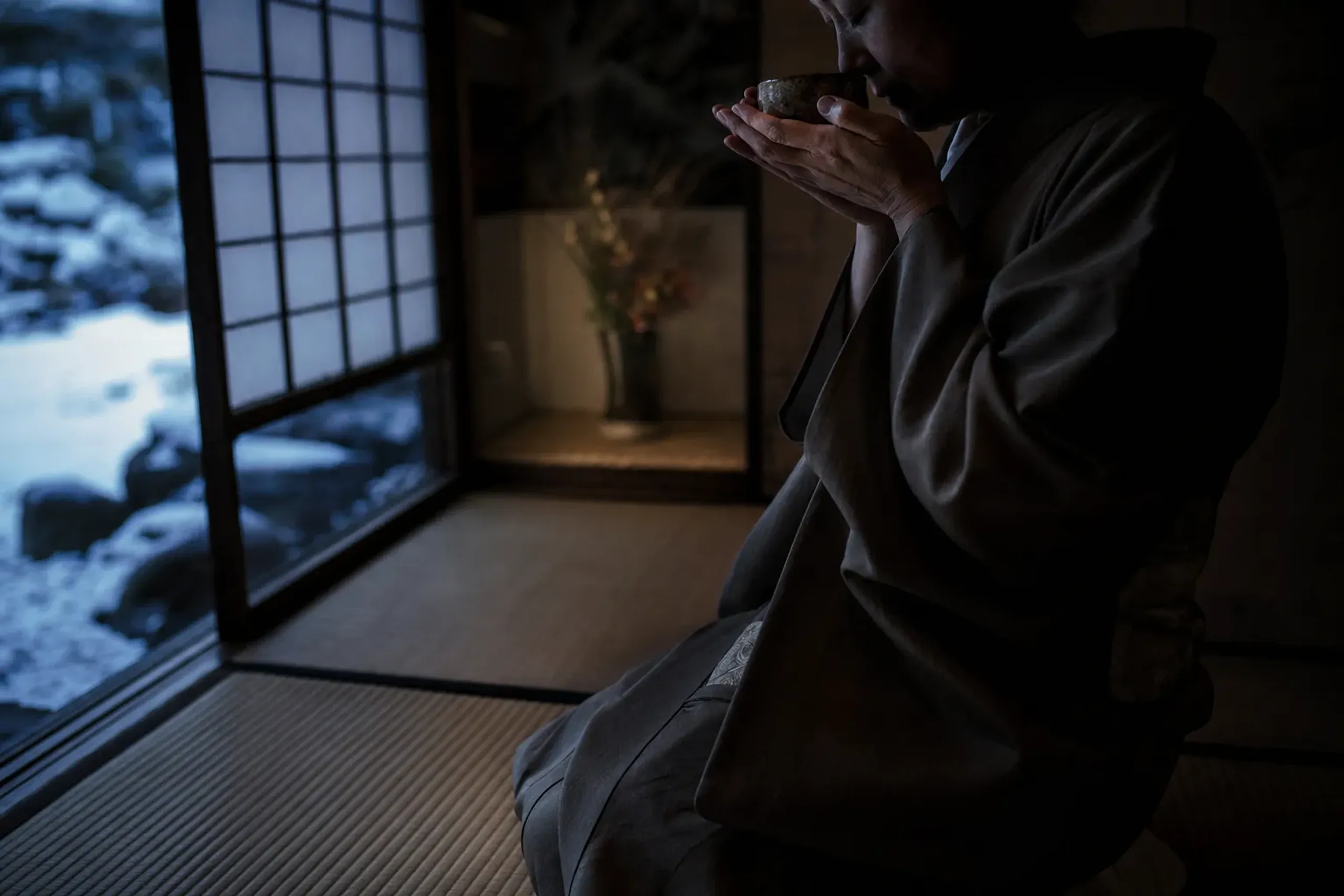 A guest kneeling in seiza on tatami, cupping the incense burner and bringing it close to listen during a kōdō session