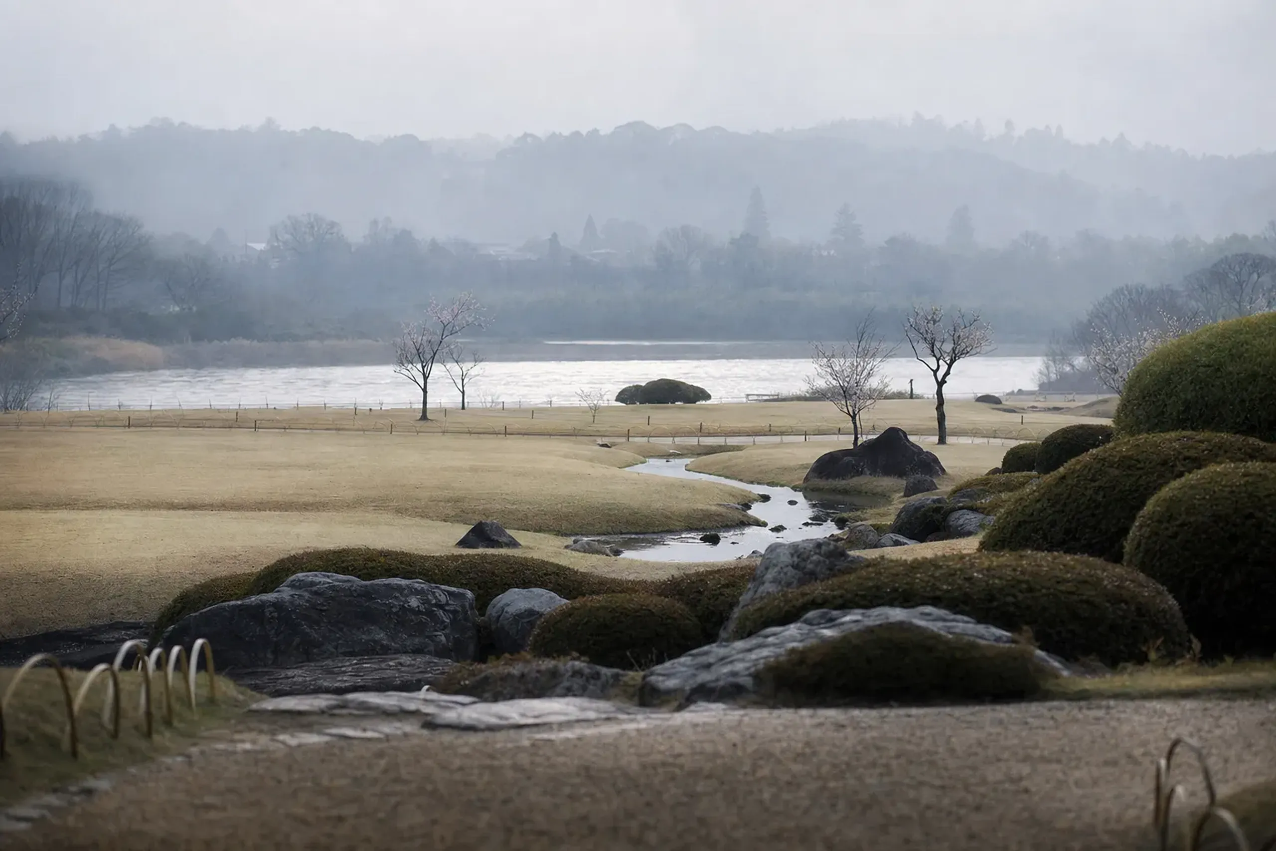 The sandbar setting of Kōraku-en in the Asahi River, its winding streams and stands of plum and cherry seen from a garden path
