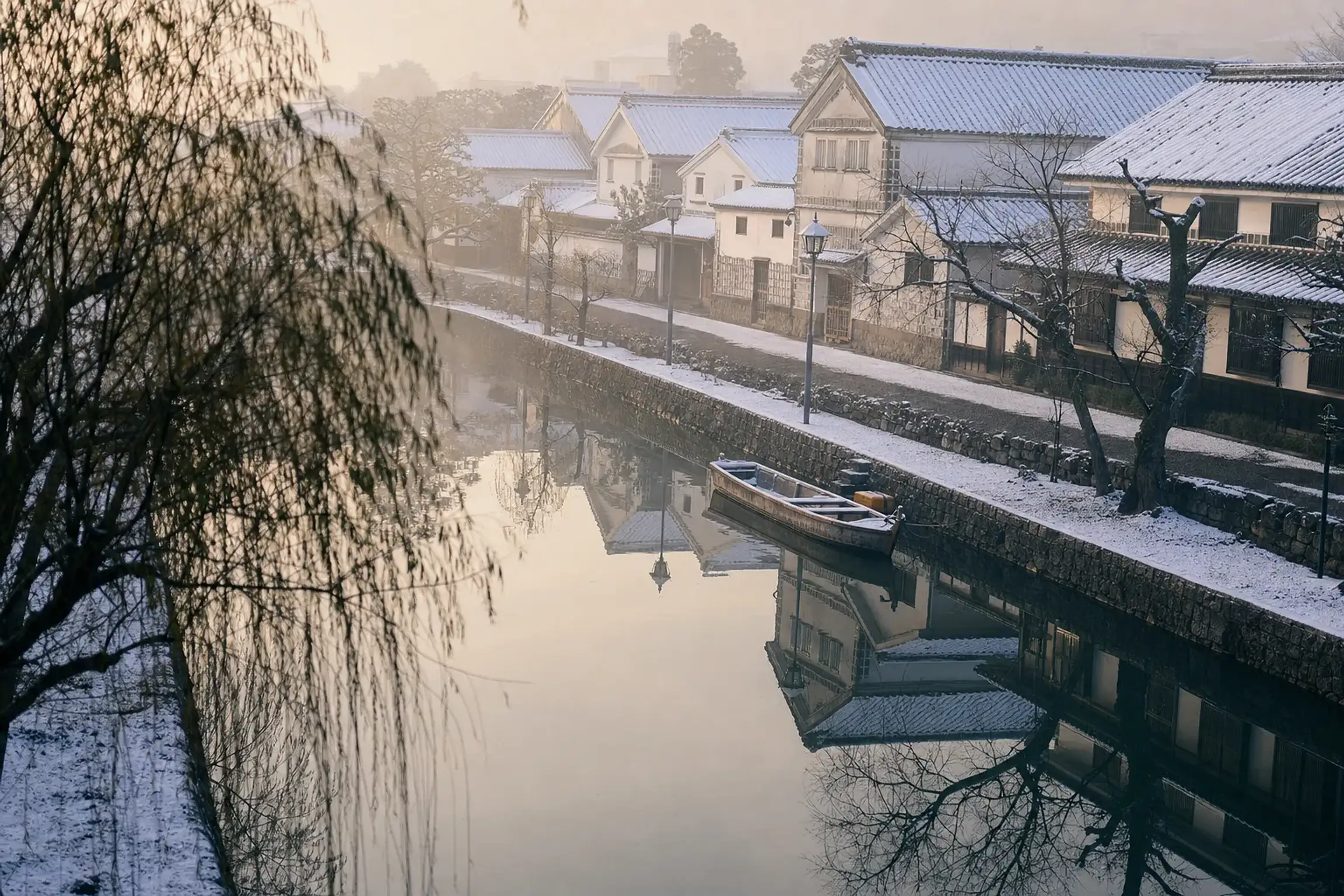 The willow-lined canal of the Kurashiki Bikan Historical Quarter with white-walled storehouses reflected in the water