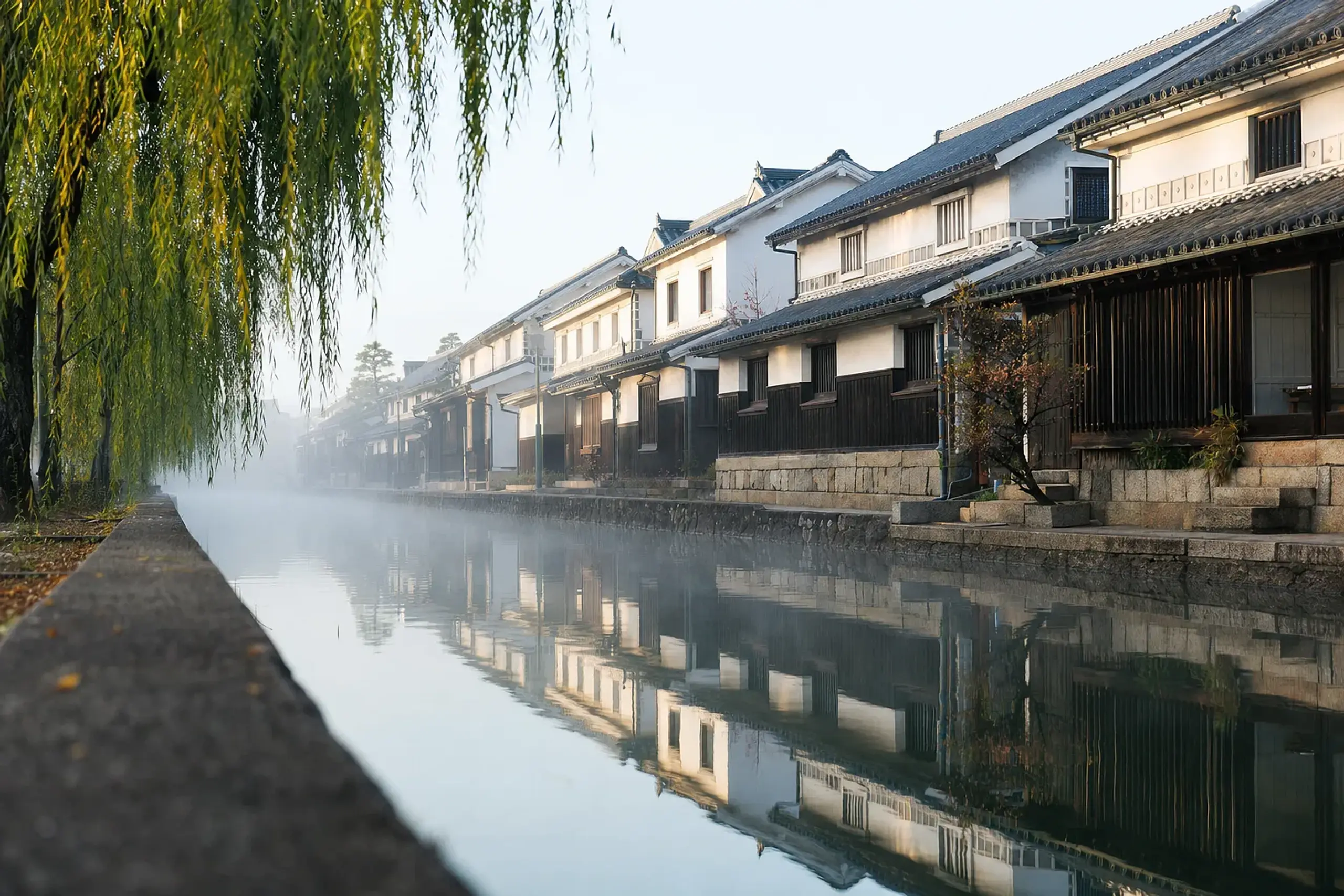 a row of Edo-period kura storehouses with black tiles and white plastered walls lining the Kurashiki River canal