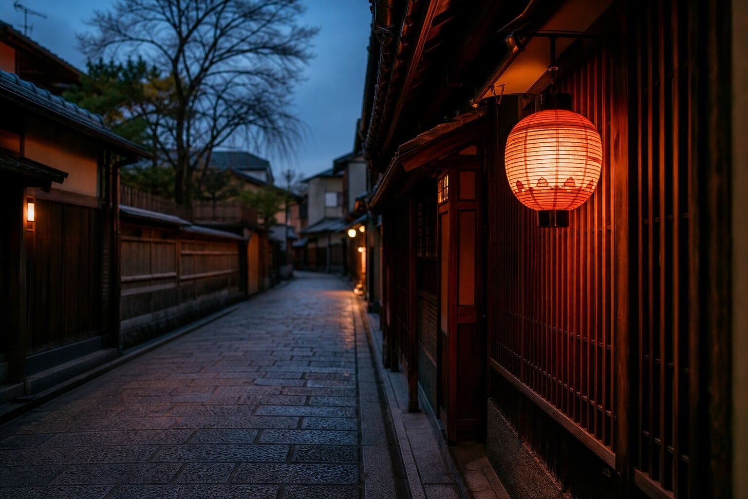 An empty stone street in Kyoto's Gion district lit by a traditional lantern at dusk.