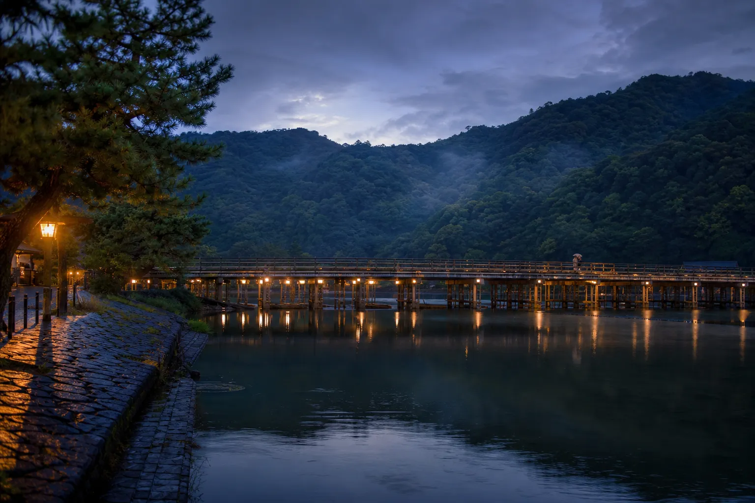 Togetsukyo Bridge over the Oi River in Arashiyama at twilight with forested hills and few visitors
