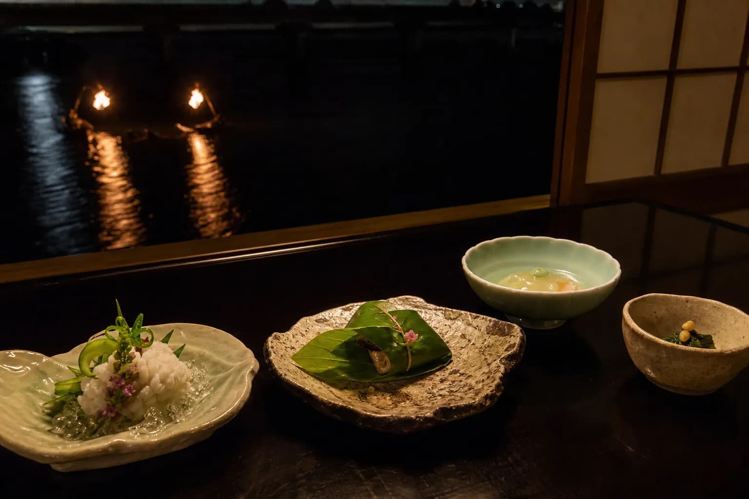 Seasonal summer kaiseki course plated on ceramic dishes beside a window overlooking the Oi River