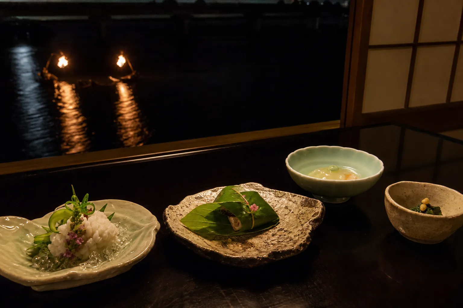 Seasonal summer kaiseki course plated on ceramic dishes beside a window overlooking the Oi River