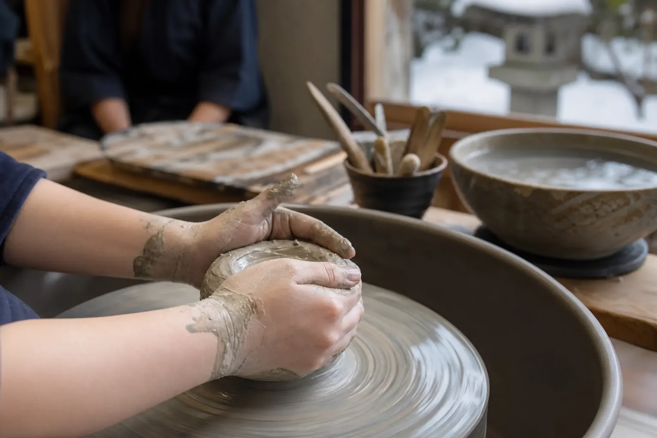 Beginner's hands shaping clay on a pottery wheel in a quiet Kyoto ceramics workshop