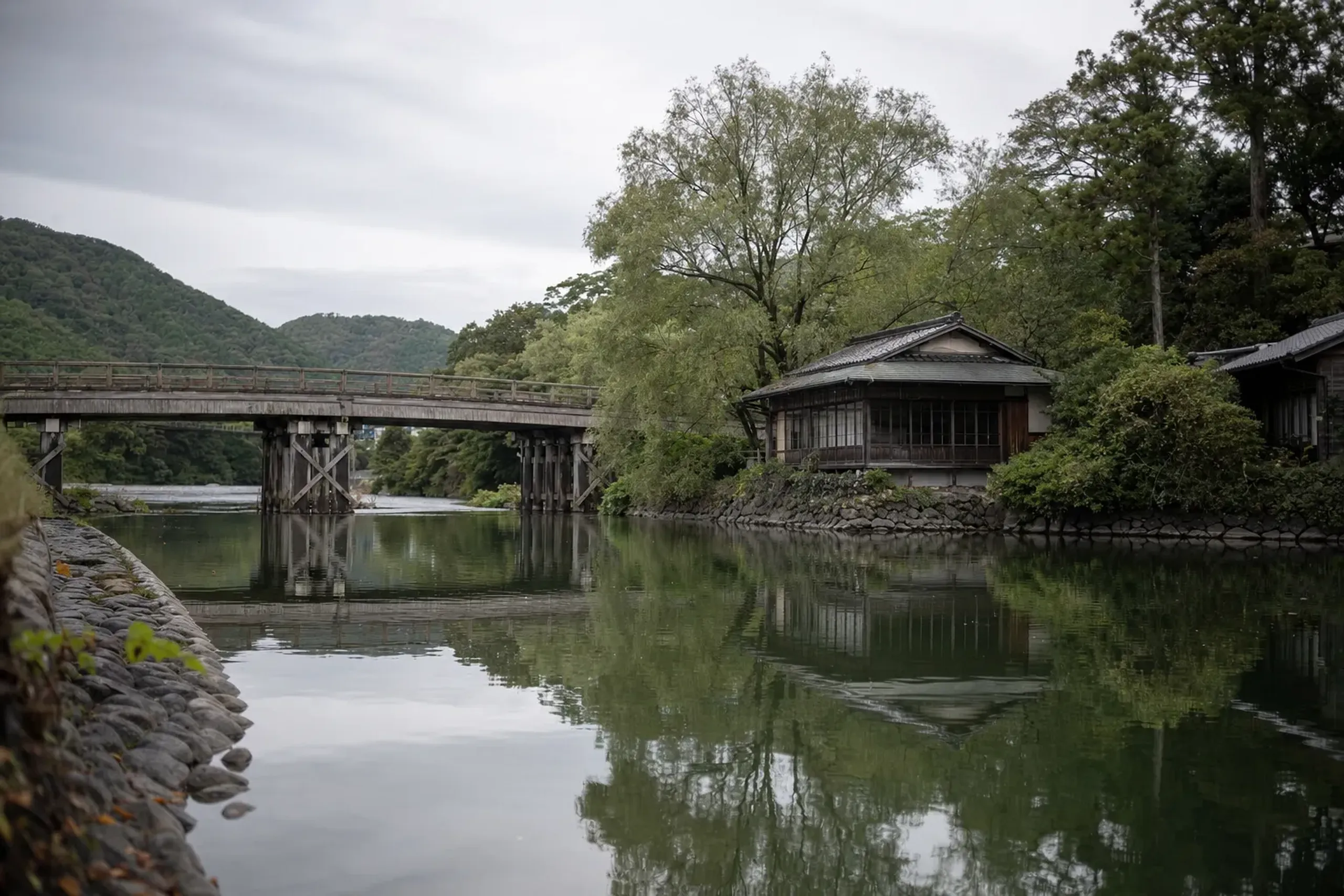 Traditional bridge over the Uji River with green banks and a wooden tea house beside the water