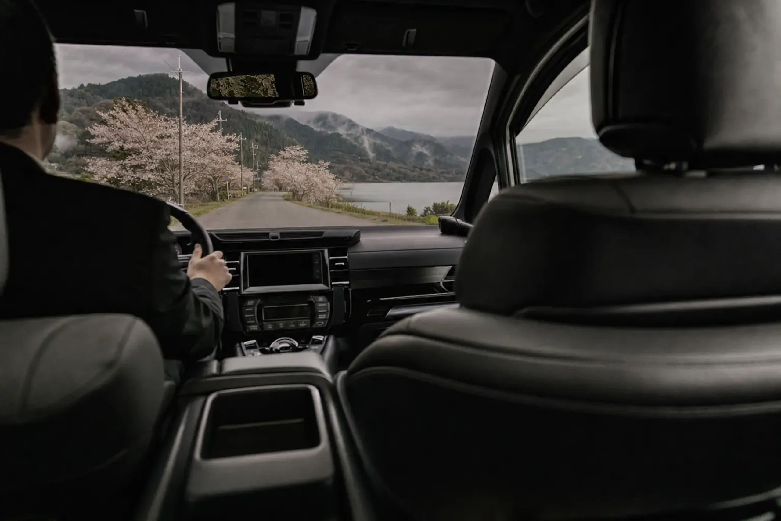 View from inside a private chauffeured vehicle travelling a rural road toward a lake outside Kyoto