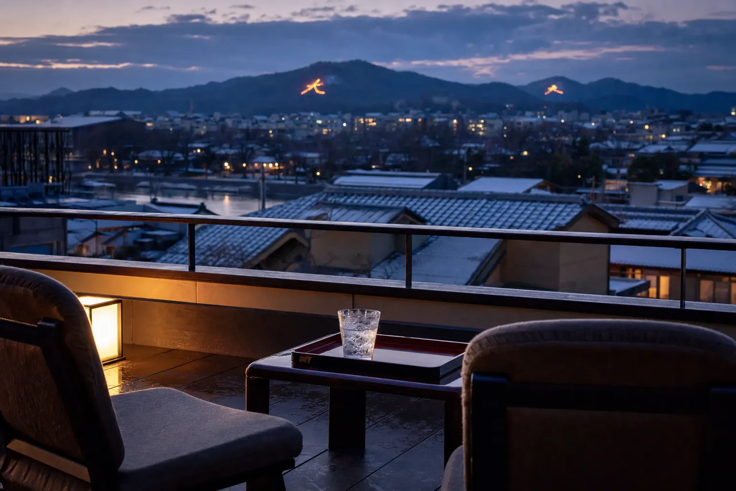 A rooftop terrace balcony overlooking Kyoto's rooftops toward the Kamo River at dusk on August 16