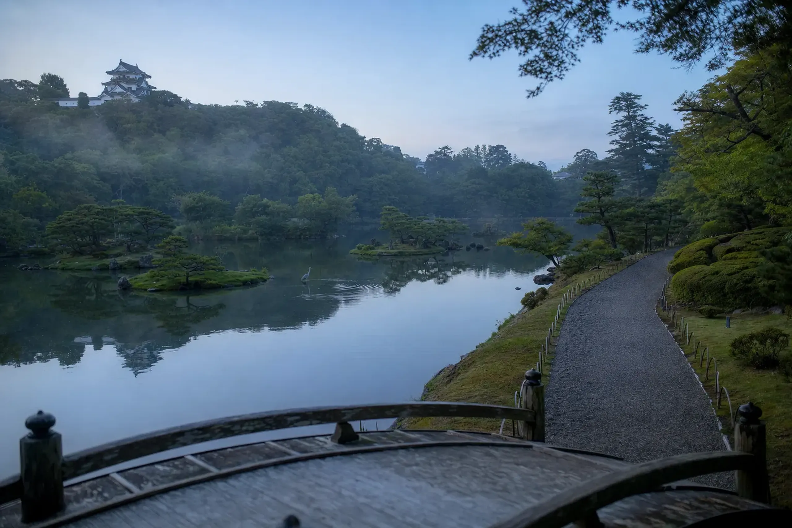 Genkyuen strolling garden at Hikone, its central pond and circular path linking four small islands, with a borrowed view of Hikone Castle's keep rising above the trees