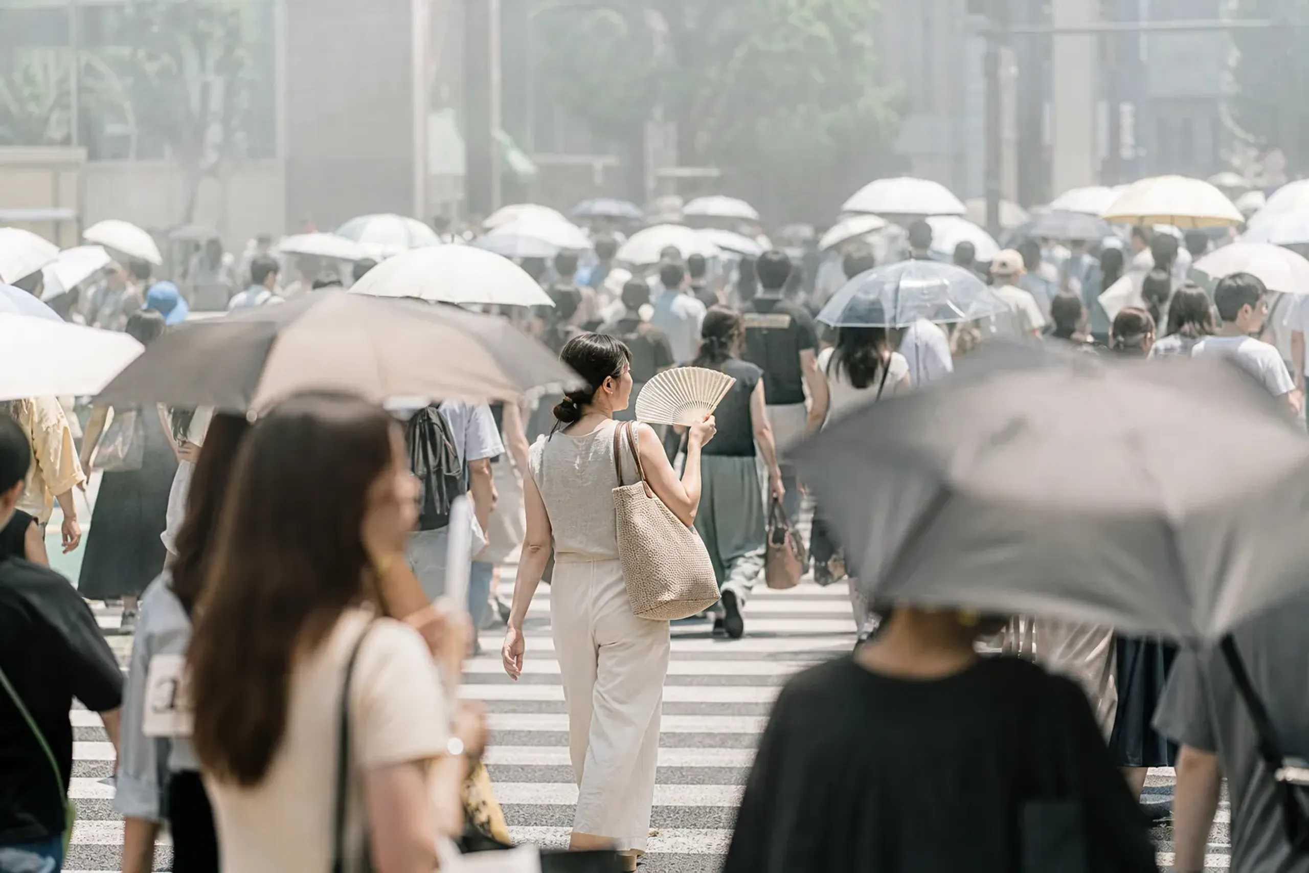Tokyo pedestrians with umbrellas and handheld fans during humid summer weather