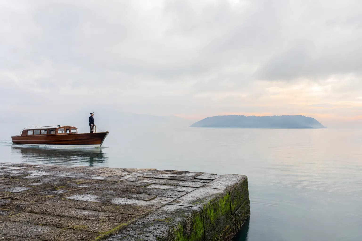a private wooden tender boat approaching a quiet stone pier at a Seto Inland Sea island port at dawn, empty of crowds