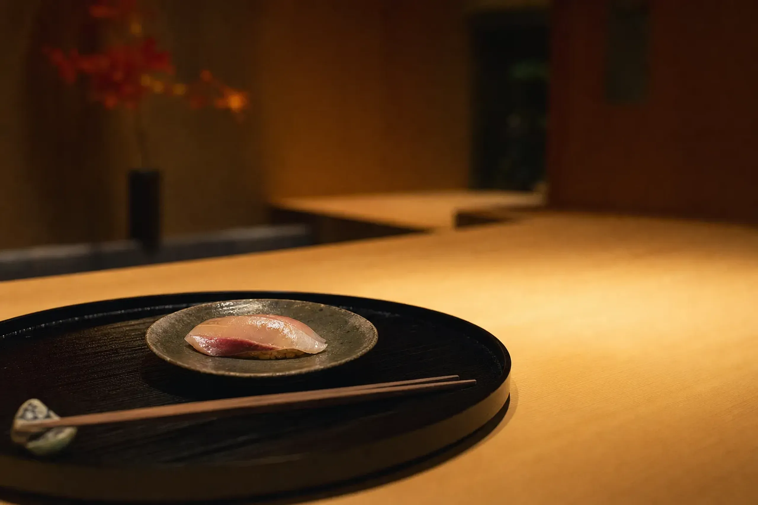 a hinoki-wood sushi counter inside a luxury Tokyo hotel, with a single lacquered serving tray and a slice of seasonal fish set on a ceramic plate