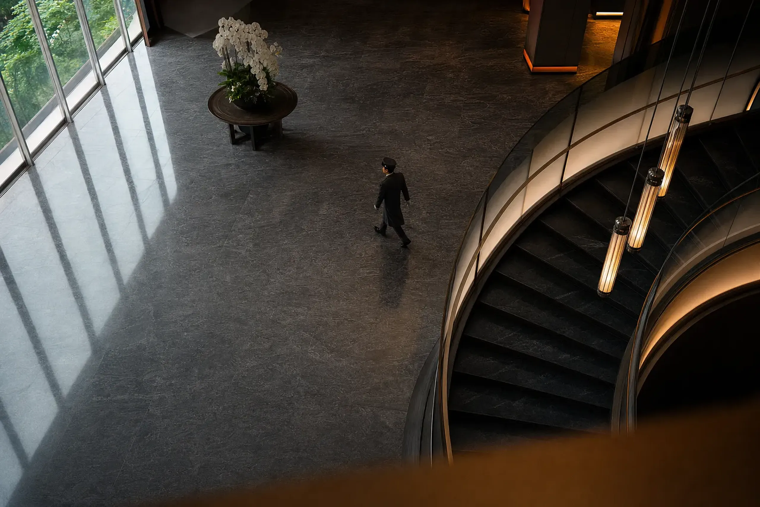 the grand marble lobby and sweeping staircase of a top-tier Three-Key Tokyo hotel tower, seen from above with reflections on polished floors