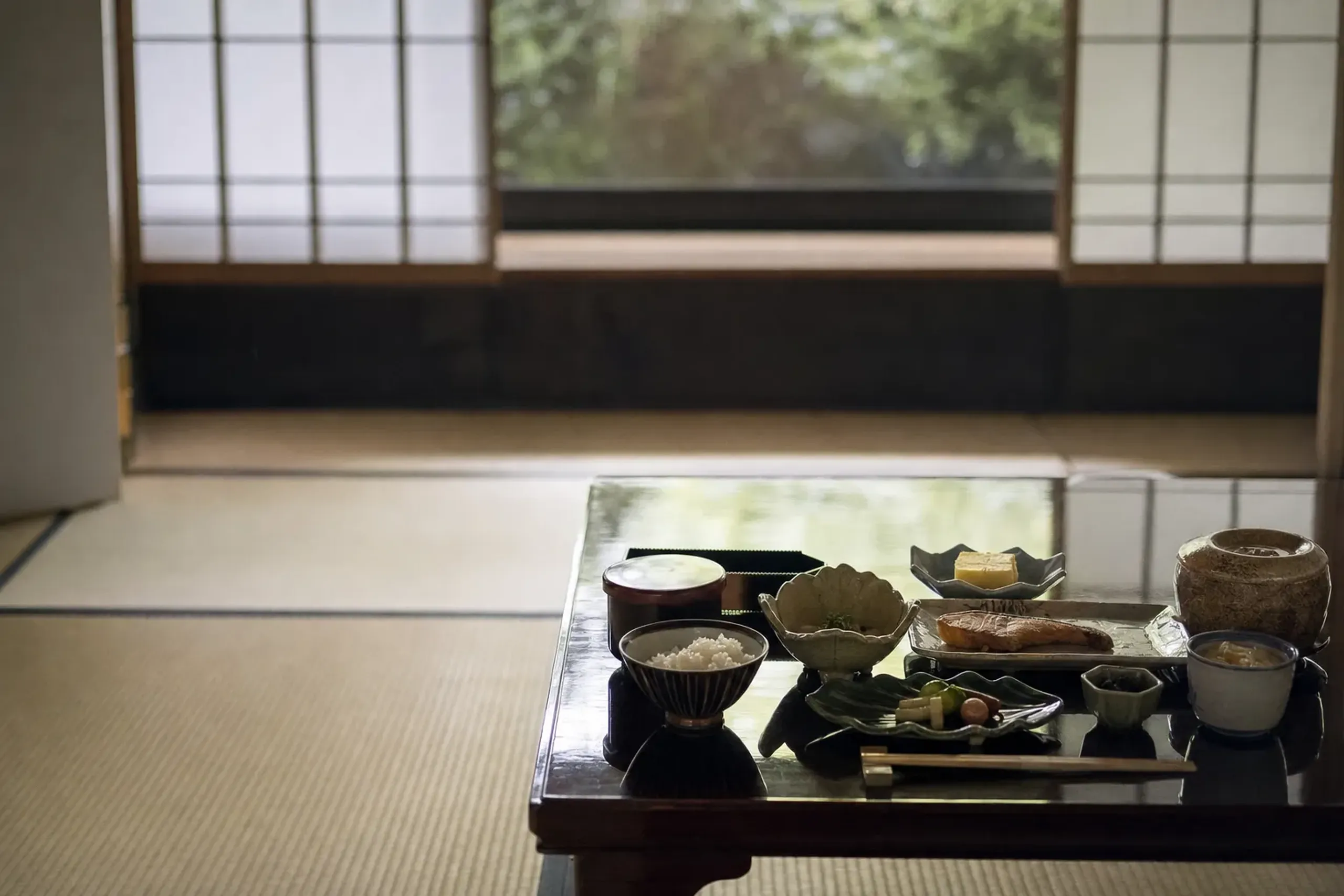 a traditional ryokan room with tatami flooring, a low lacquered table set for kaiseki breakfast, shoji screens, and seasonal ceramics arranged with precise joinery visible in the wooden beams