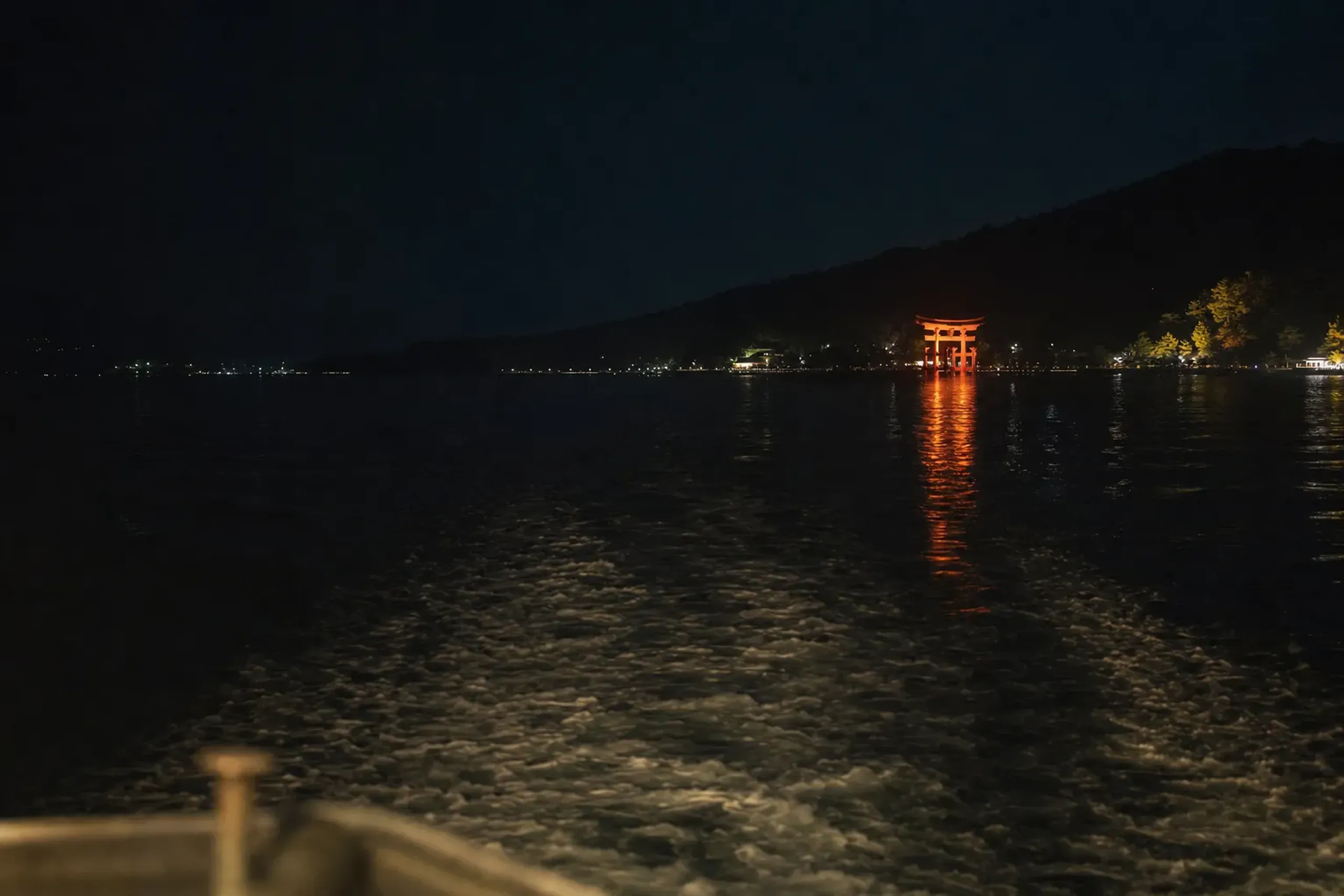the Miyajima ferry crossing the dark waters of the Seto Inland Sea at night, with the illuminated Great Torii in the distance