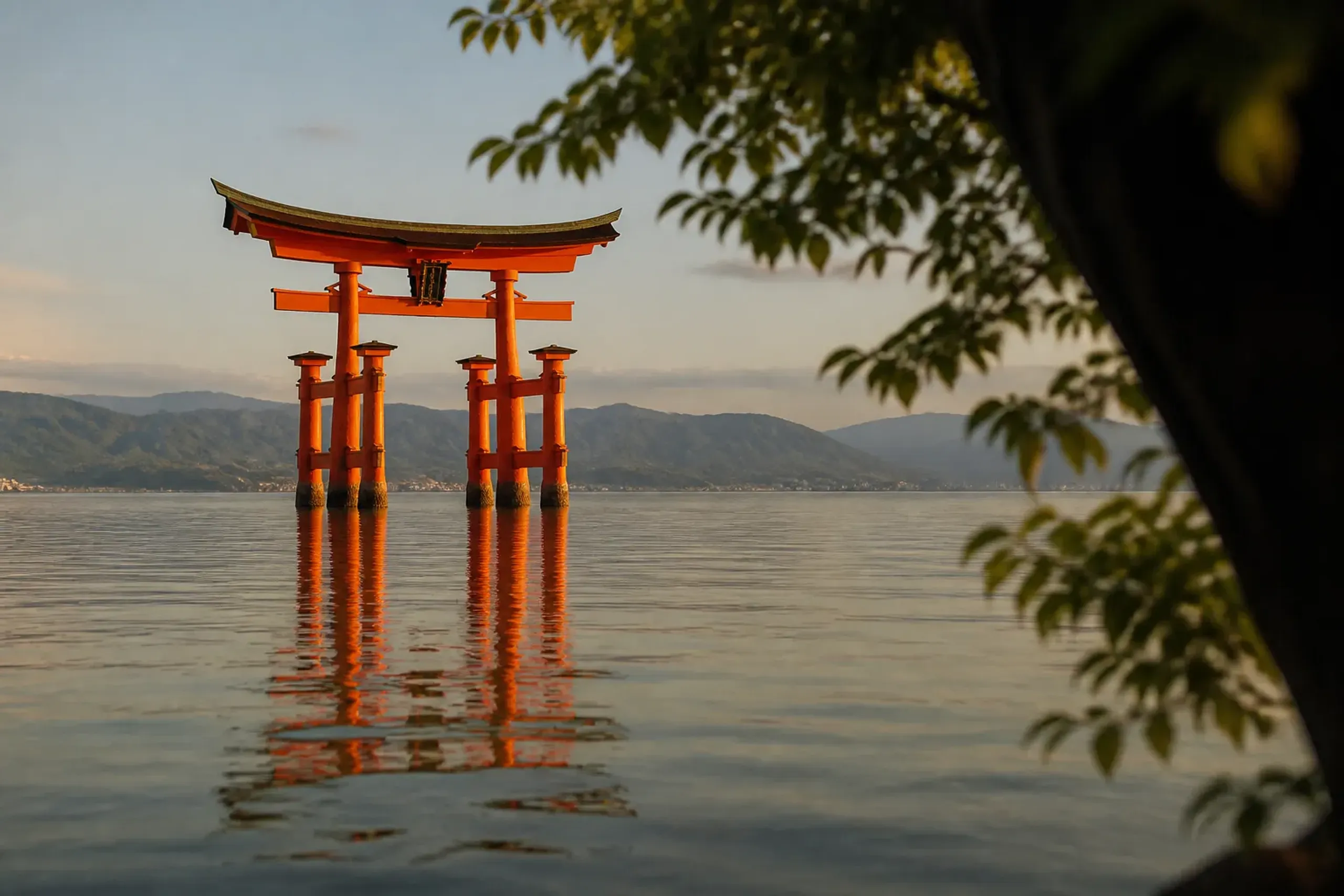 The great vermilion torii of Itsukushima Shrine standing offshore in open water at high tide, with the shrine's corridors reflected in the sea beneath the vermilion pillars, Miyajima