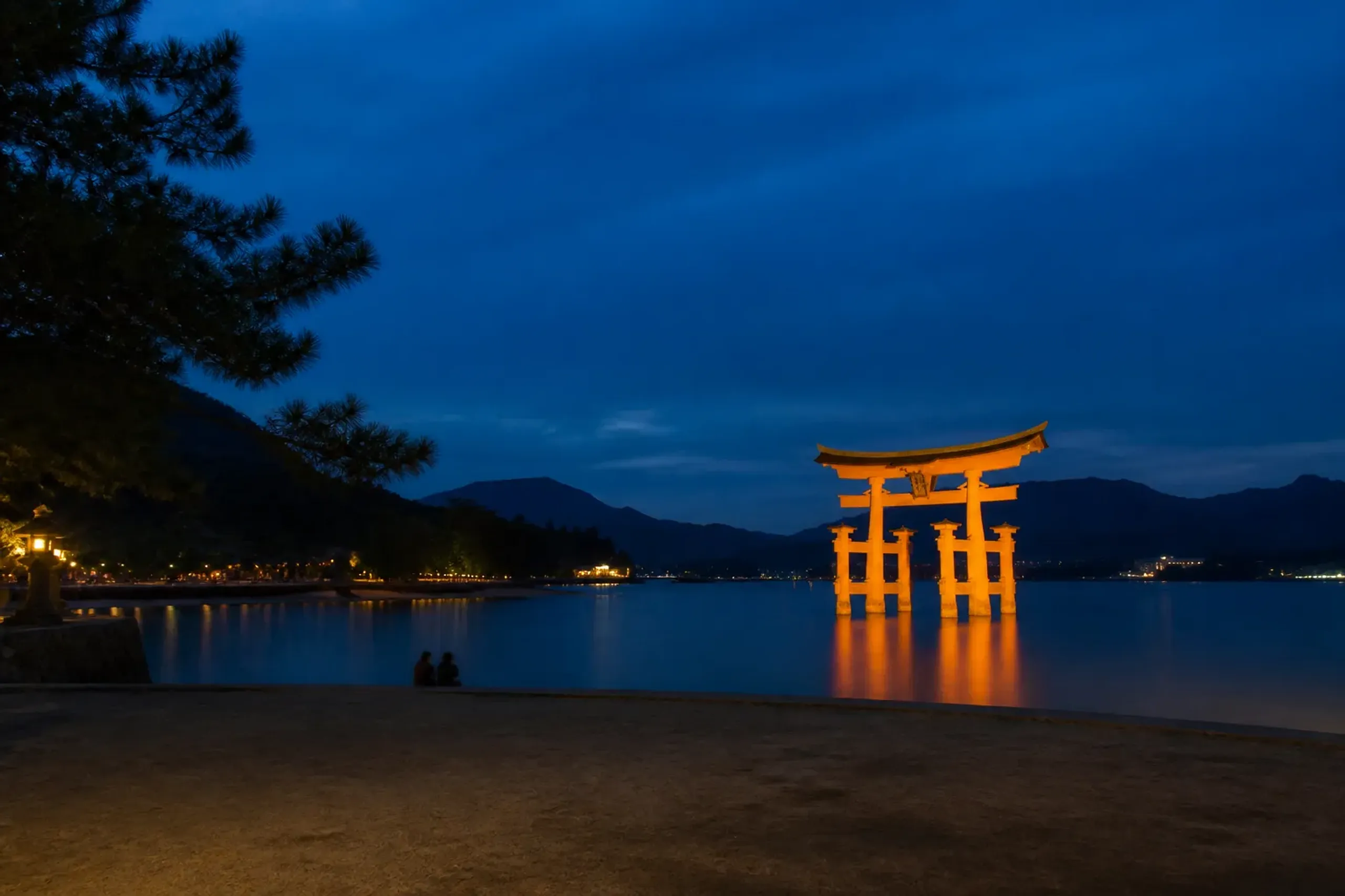 Illuminated Great Torii on Miyajima at dusk with reflections on dark water and few visitors