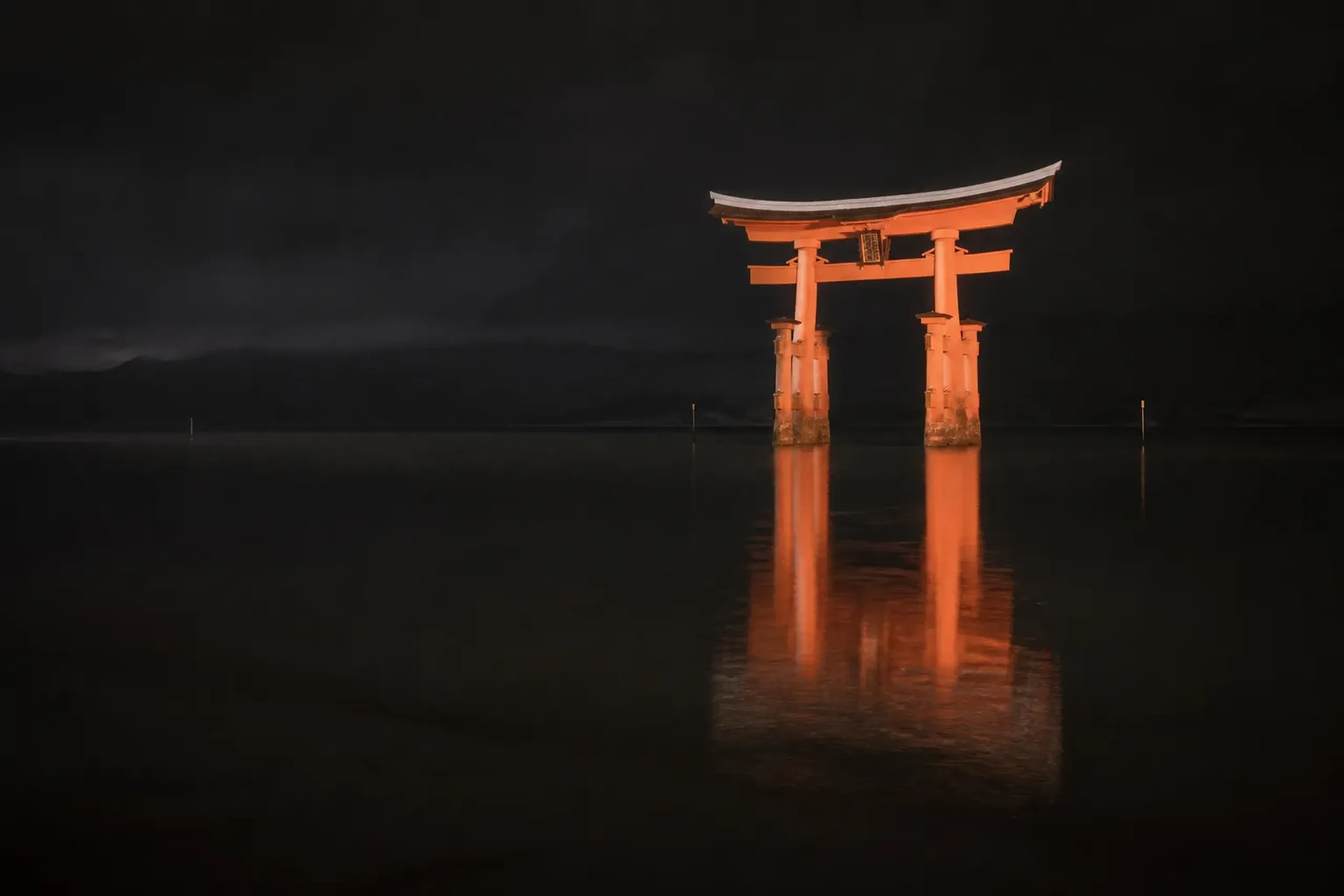 the illuminated Great Torii of Itsukushima Shrine glowing vermilion against black water at high tide after nightfall