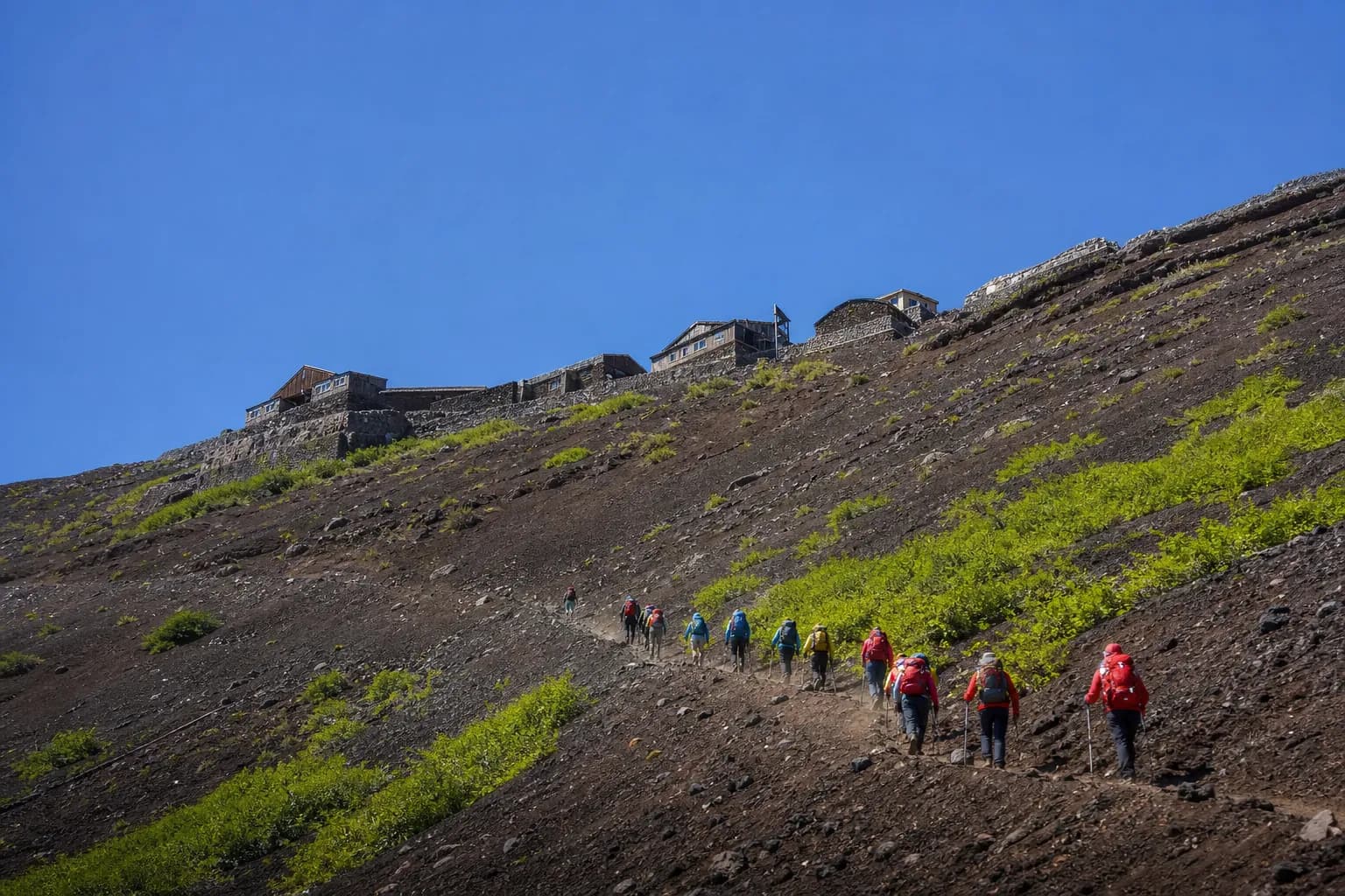 Hikers climbing the Yoshida Trail switchbacks on Mount Fuji with mountain huts along the ridge