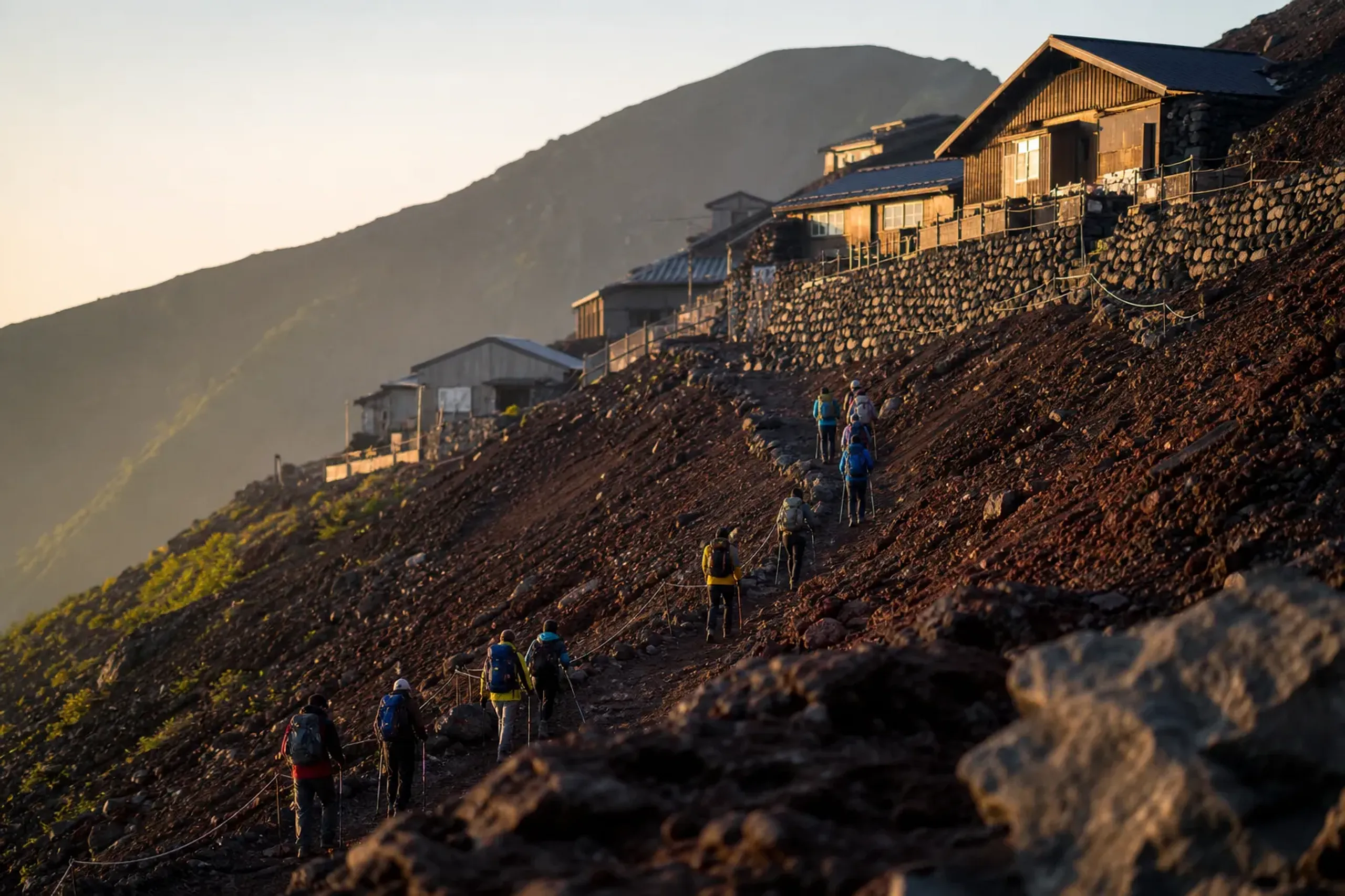 Hikers climbing the Yoshida Trail switchbacks on Mount Fuji with mountain huts along the ridge