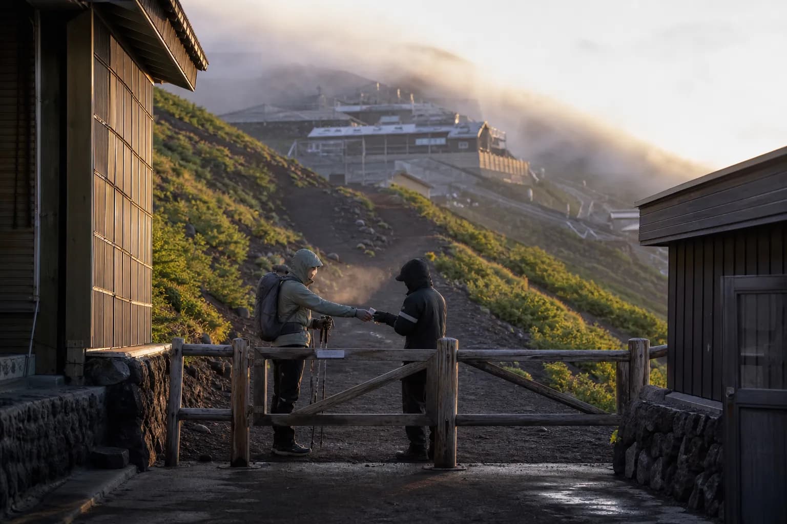 The controlled entry gate at the Yoshida Trail 5th Station on the Yamanashi side of Mt. Fuji, with the volcanic scree path and clustered wooden mountain huts stretching up the slope behind it