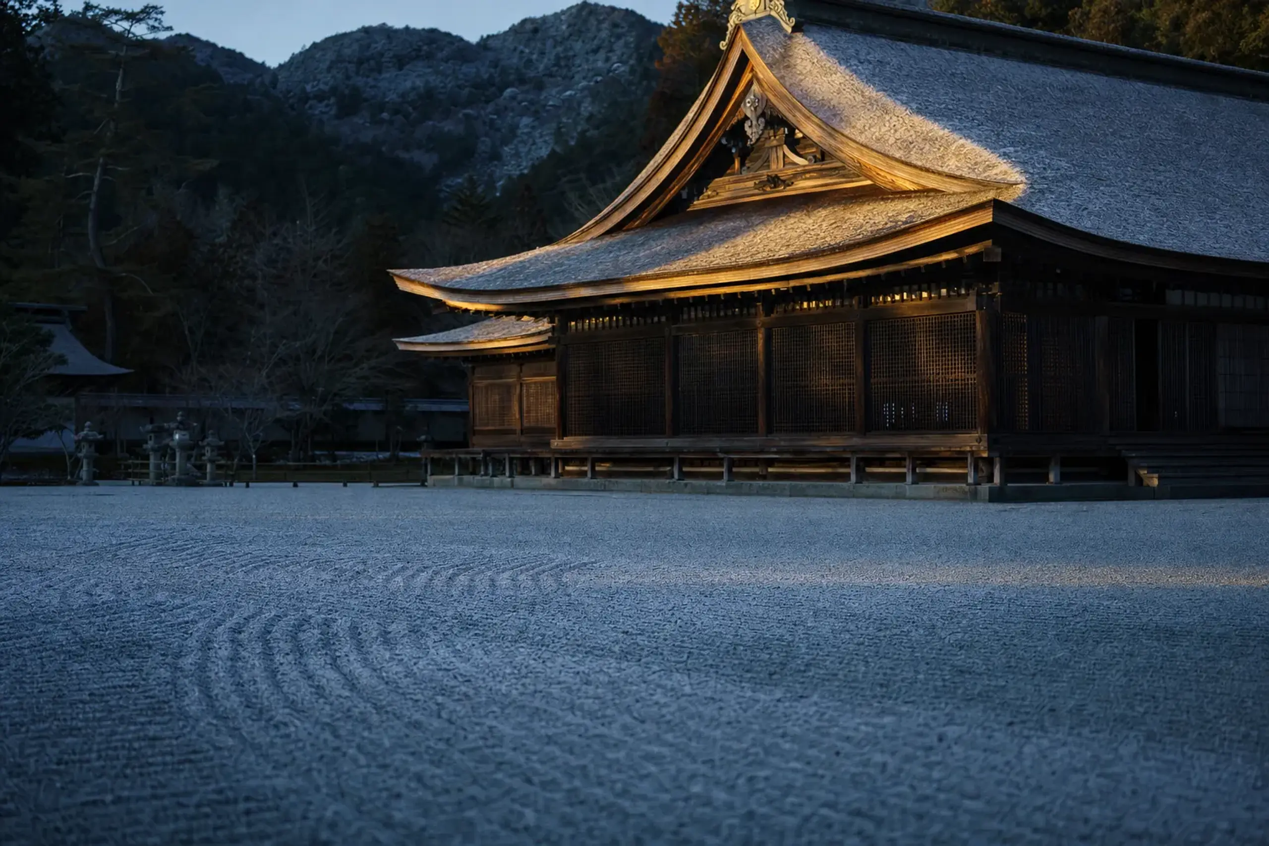 Sunlight catching the curved cypress-bark rooflines of Hetsu-gū's main hall as shadow falls across the orderly gravel precinct