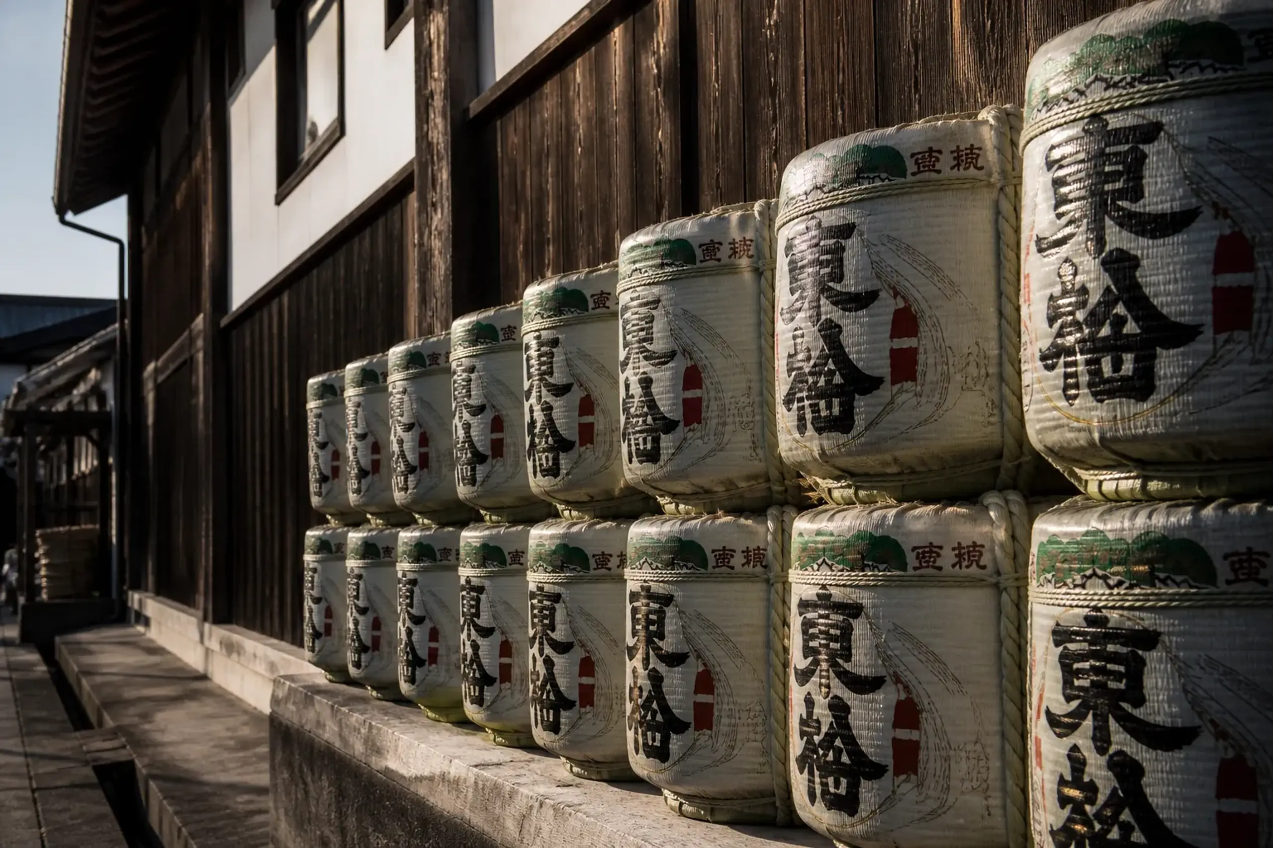 Wooden sake barrels stacked outside a Nada-Gogo brewery in Kobe under crisp winter light during the cold brewing season