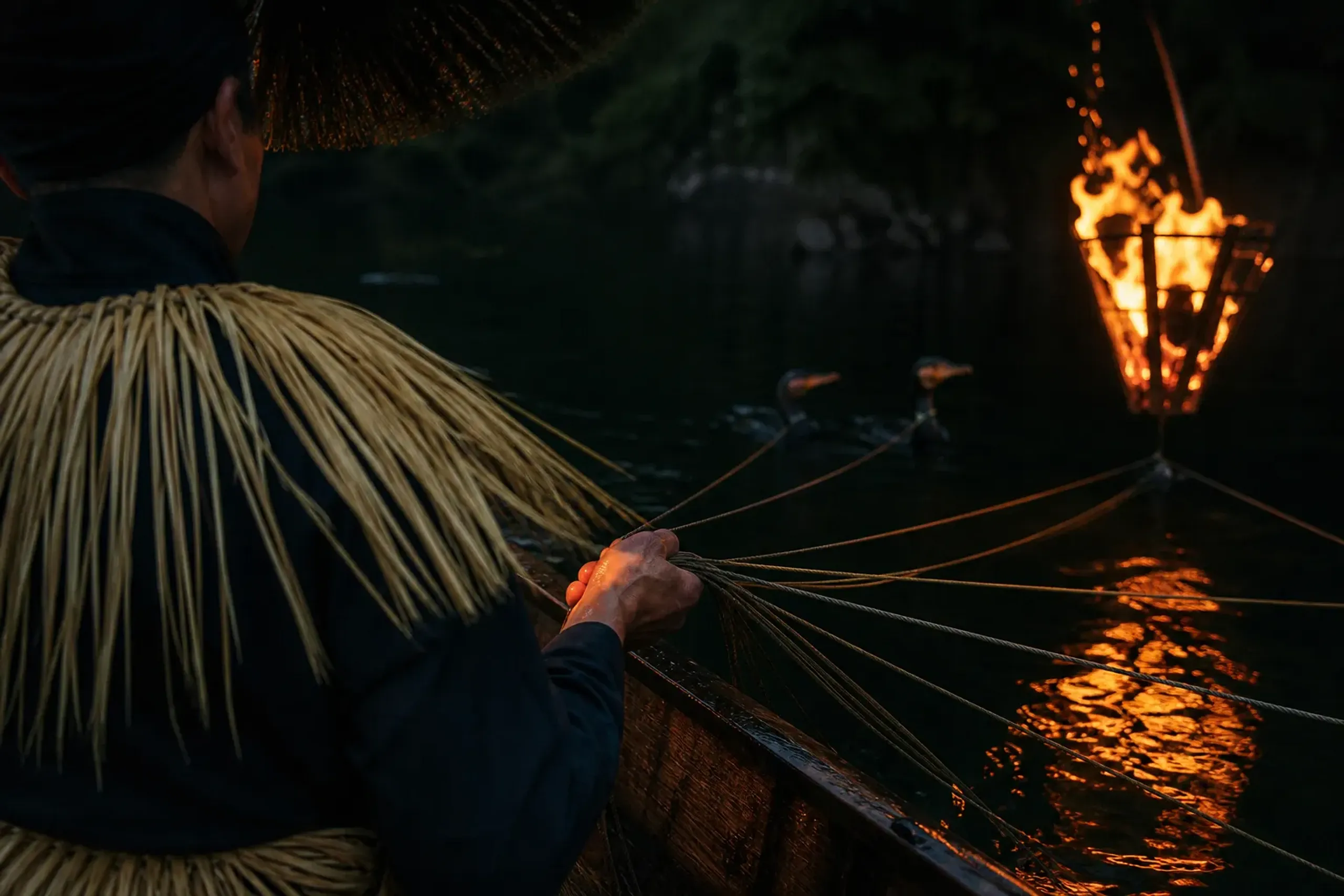 Cormorant fishing master on a wooden boat holding hand ropes during ukai on the Nagara River