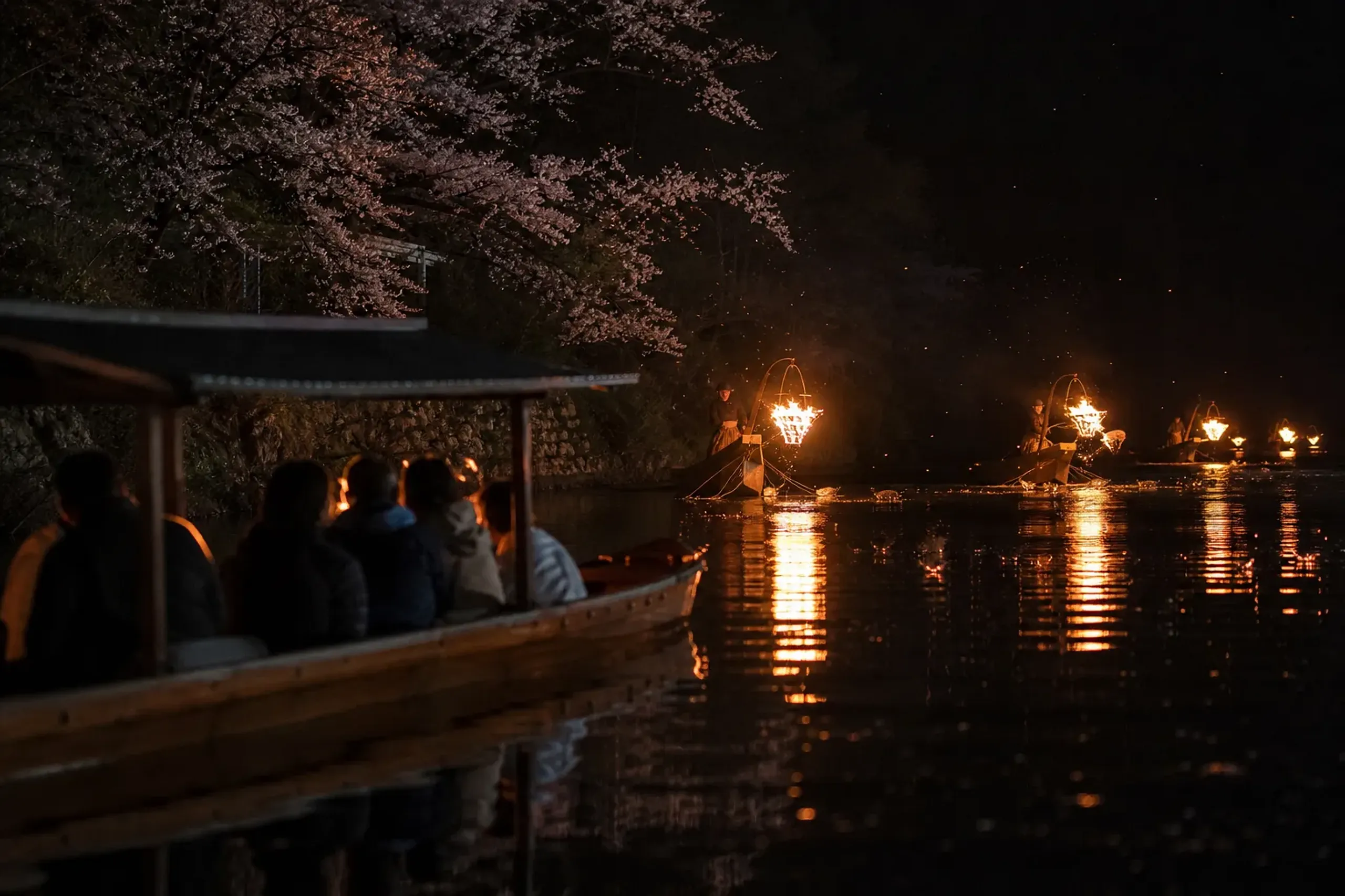 Guests watching ukai boats with torch flames on the Nagara River at night