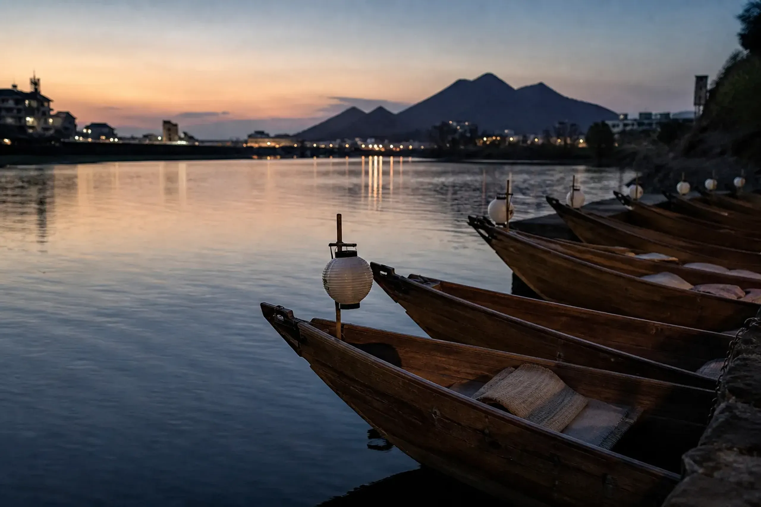 empty wooden ukai spectator boats moored along the Nagara River bank at dusk before the evening's fishing begins