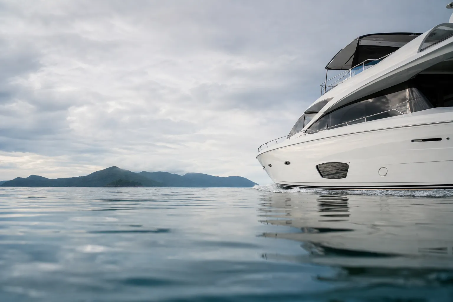A sleek, modern white yacht sailing on calm blue waters with green islands in the background.