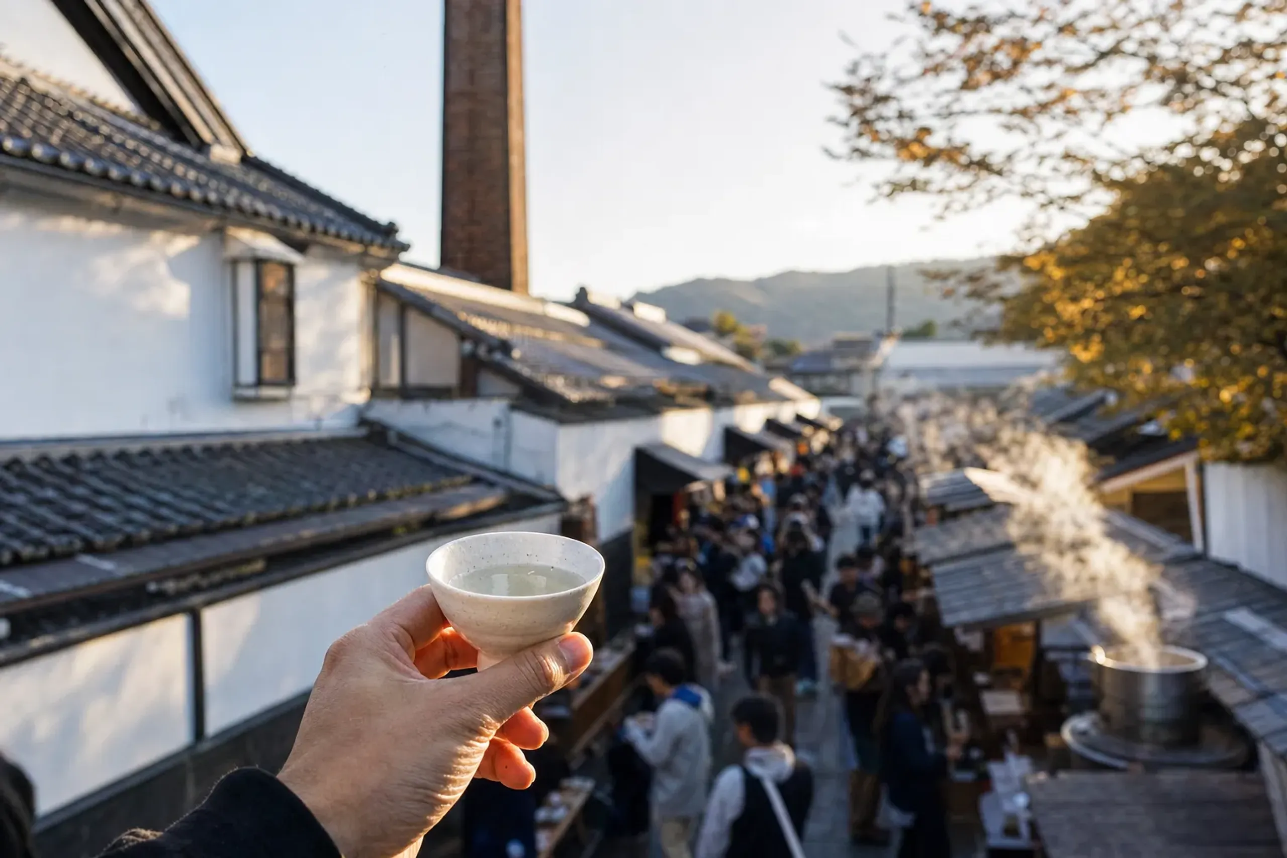 the crowded brewery street of Saijo during the October Sake Festival, with tasting stalls set among the brick chimneys and white-walled kura