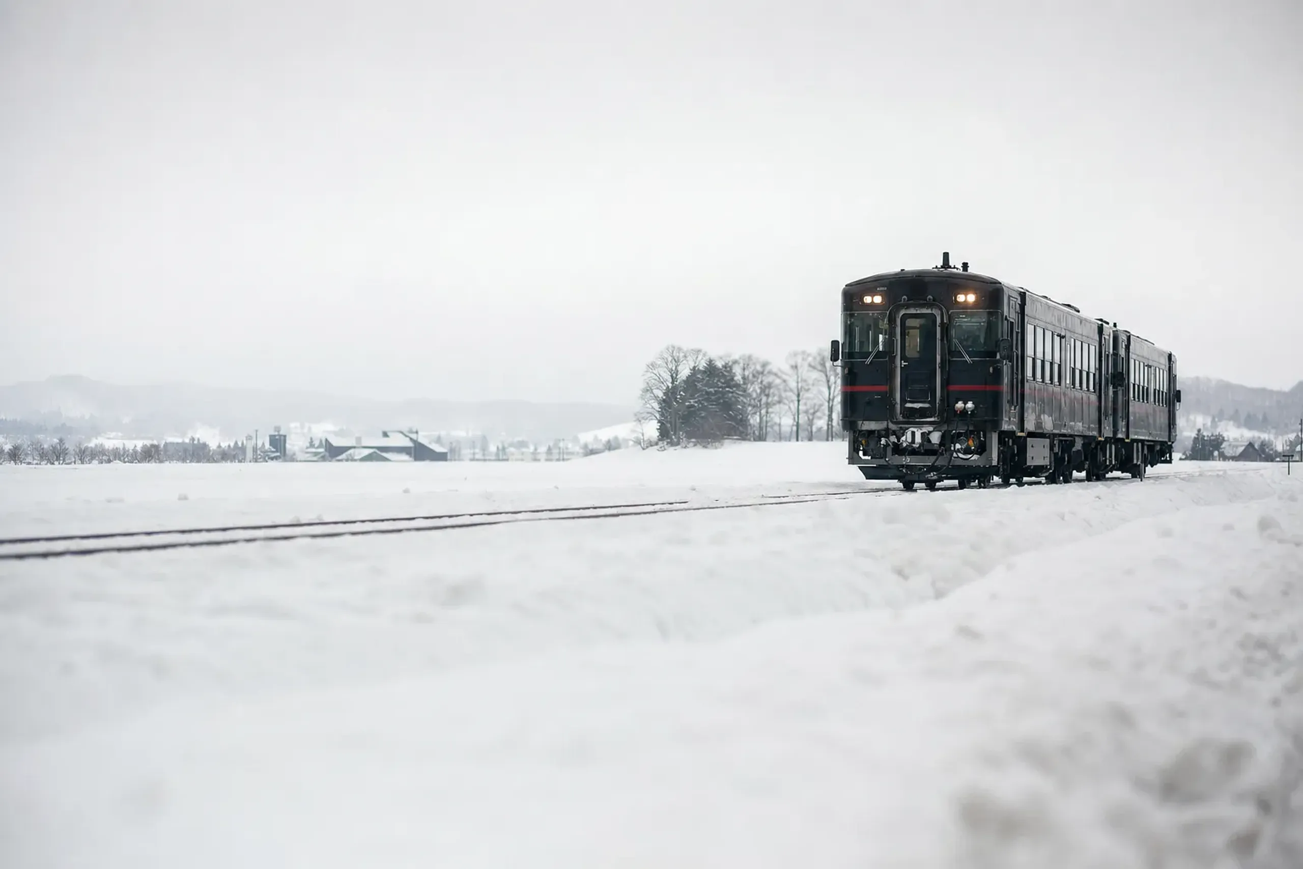 A snow-covered rural Niigata train line running between brewery stops, tracks cutting through white snow-country landscape